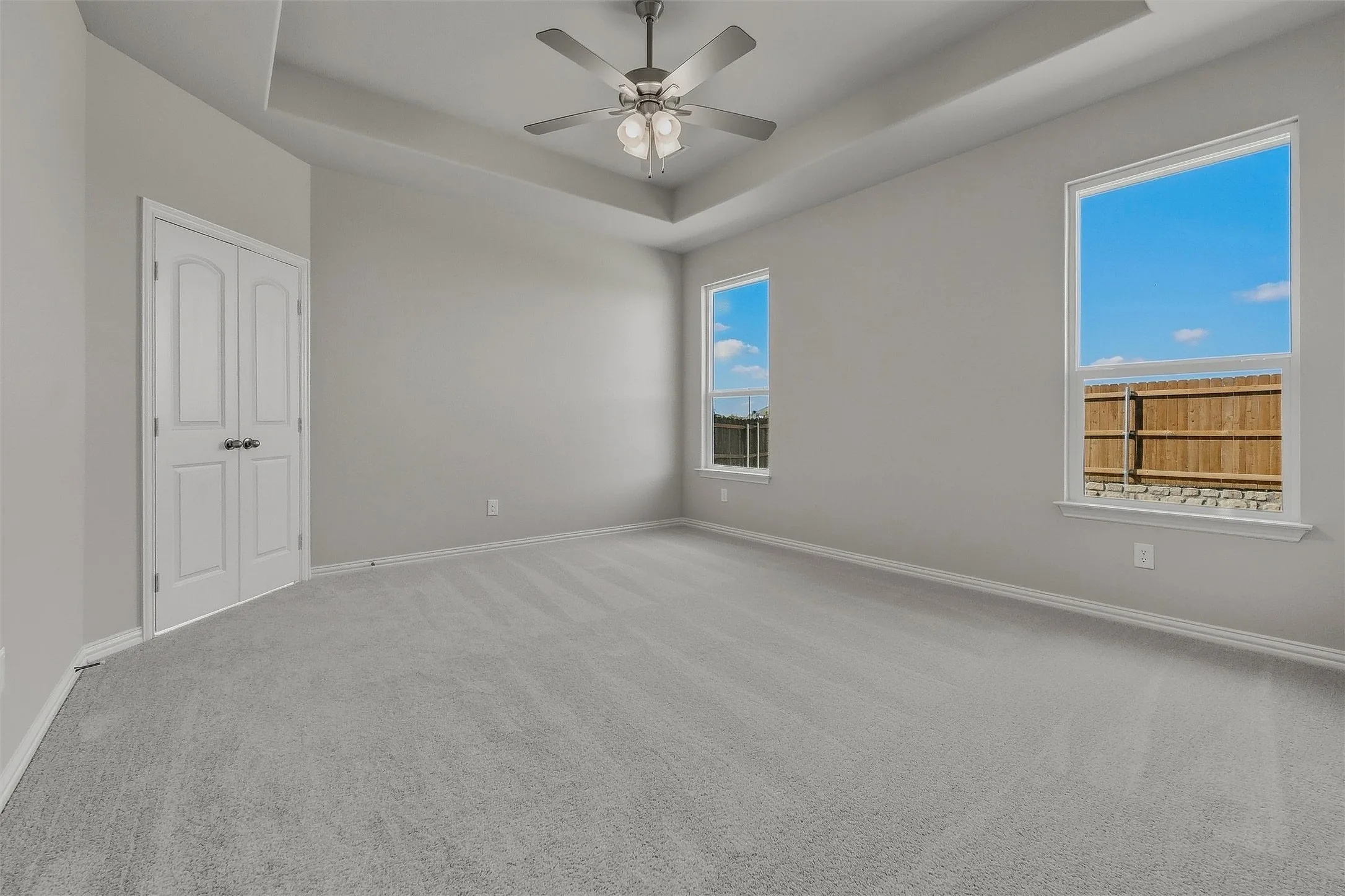 Tray ceiling with a ceiling fan, dual windows, and light gray wall paint