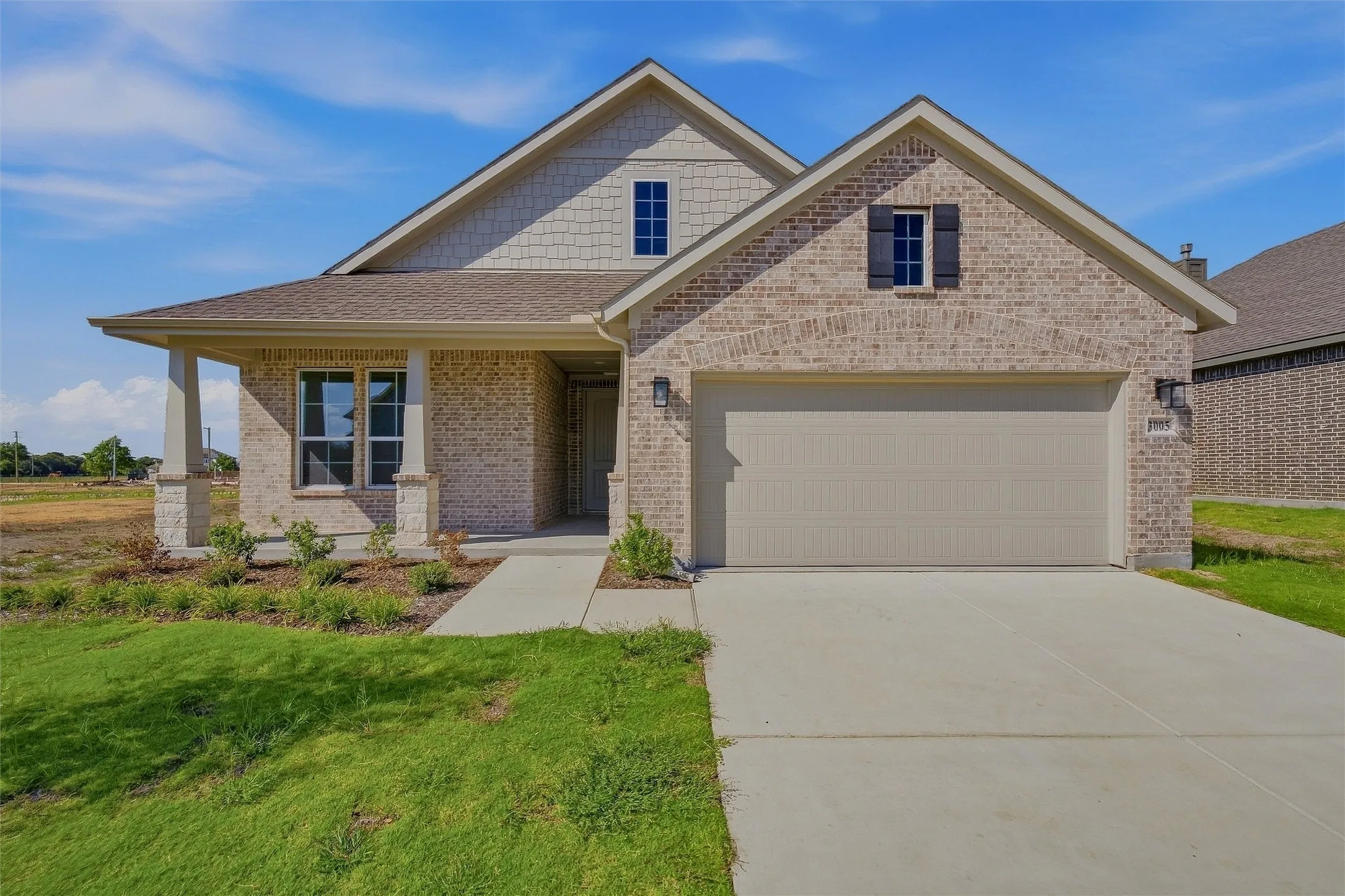 Brick exterior with complementary siding, covered entry porch, attached garage, and established landscaping