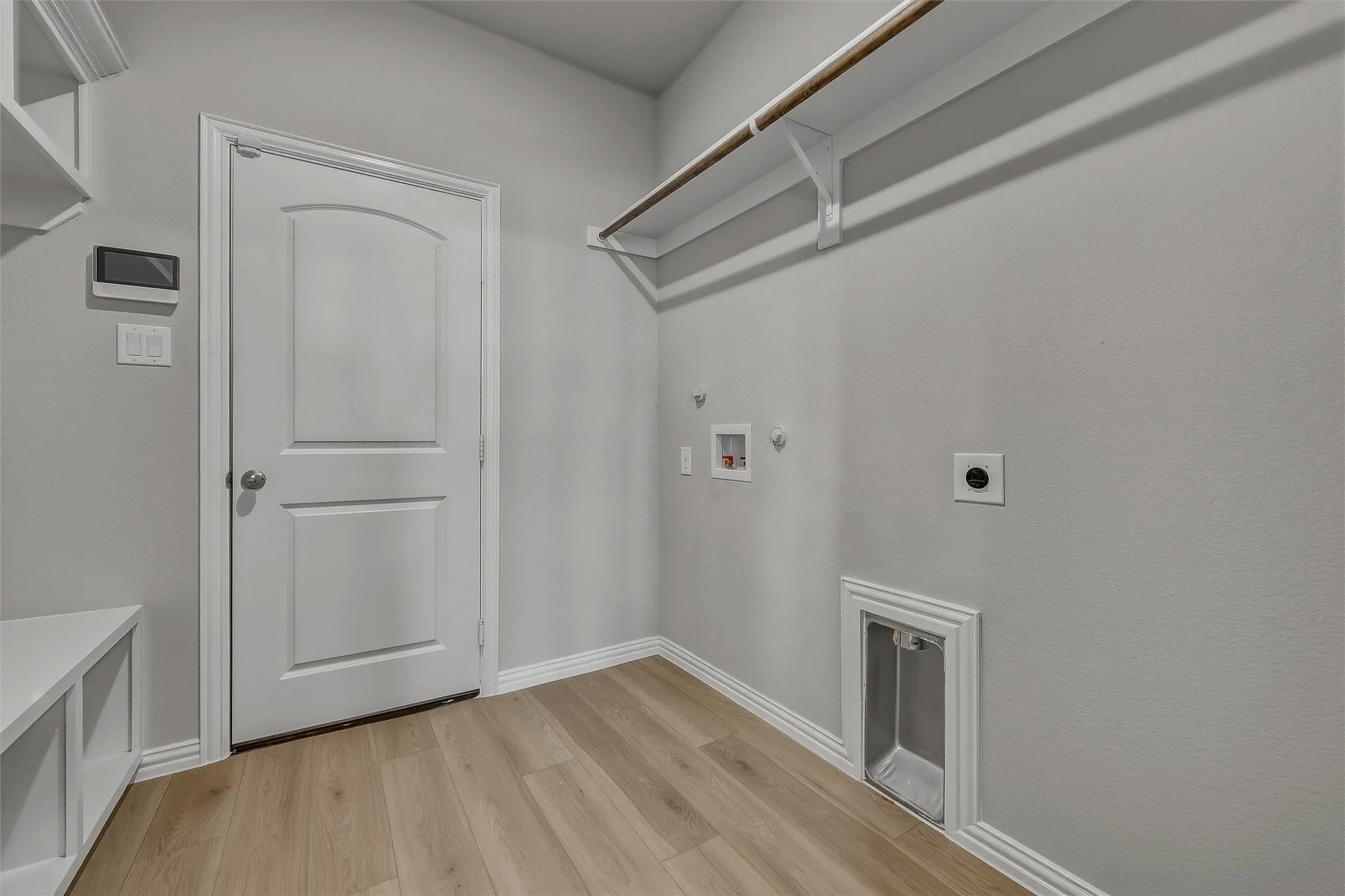 Utility space featuring wood-finish flooring, built-in shelving, wall-mounted hanging rod, and laundry hookups