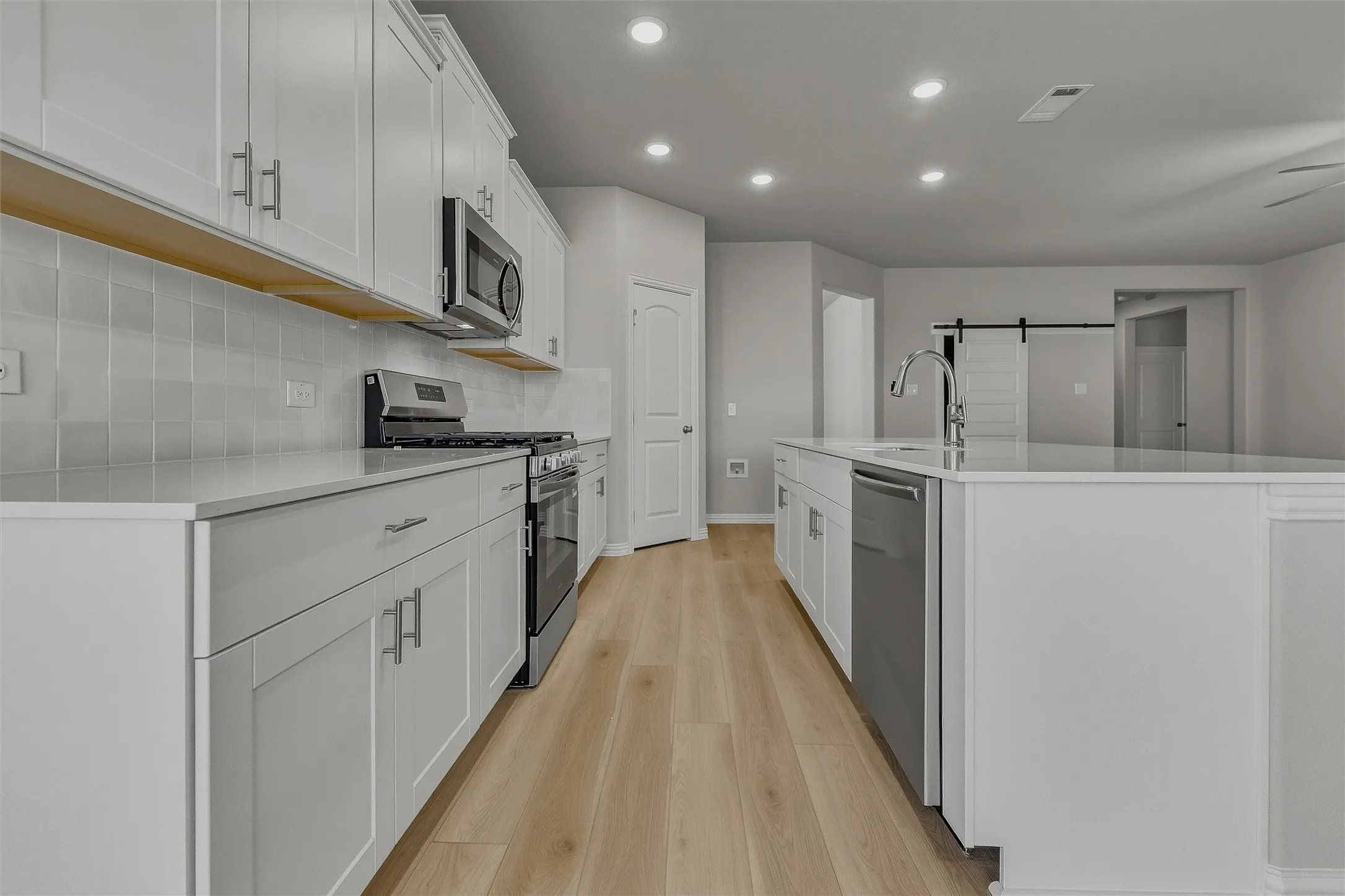 Contemporary kitchen featuring white cabinetry, stainless steel appliances, a center island with a sink, wood-finish flooring, and recessed lighting
