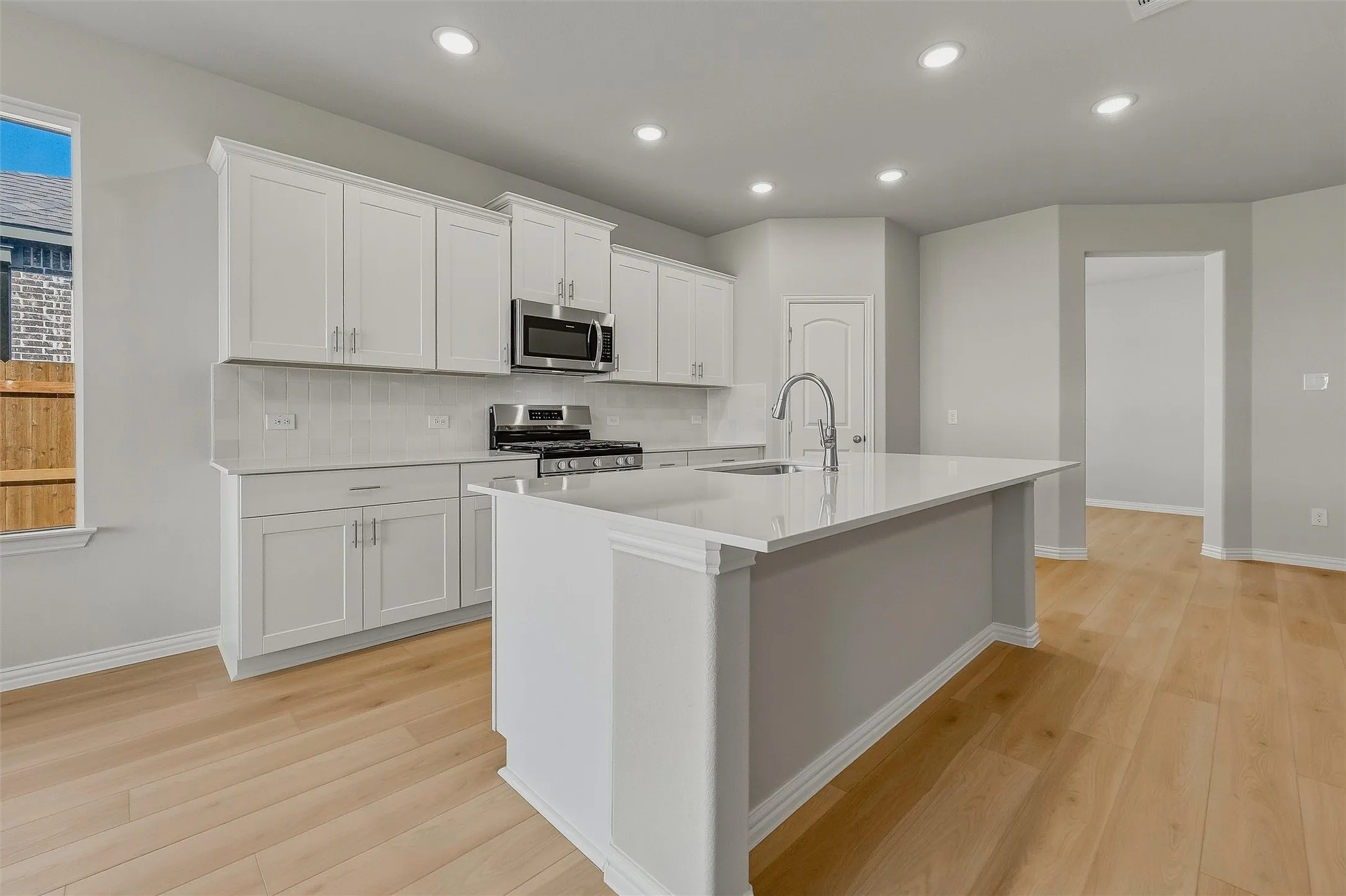 Kitchen featuring white cabinetry, a large center island with a sink, stainless steel appliances, and light wood-finish flooring