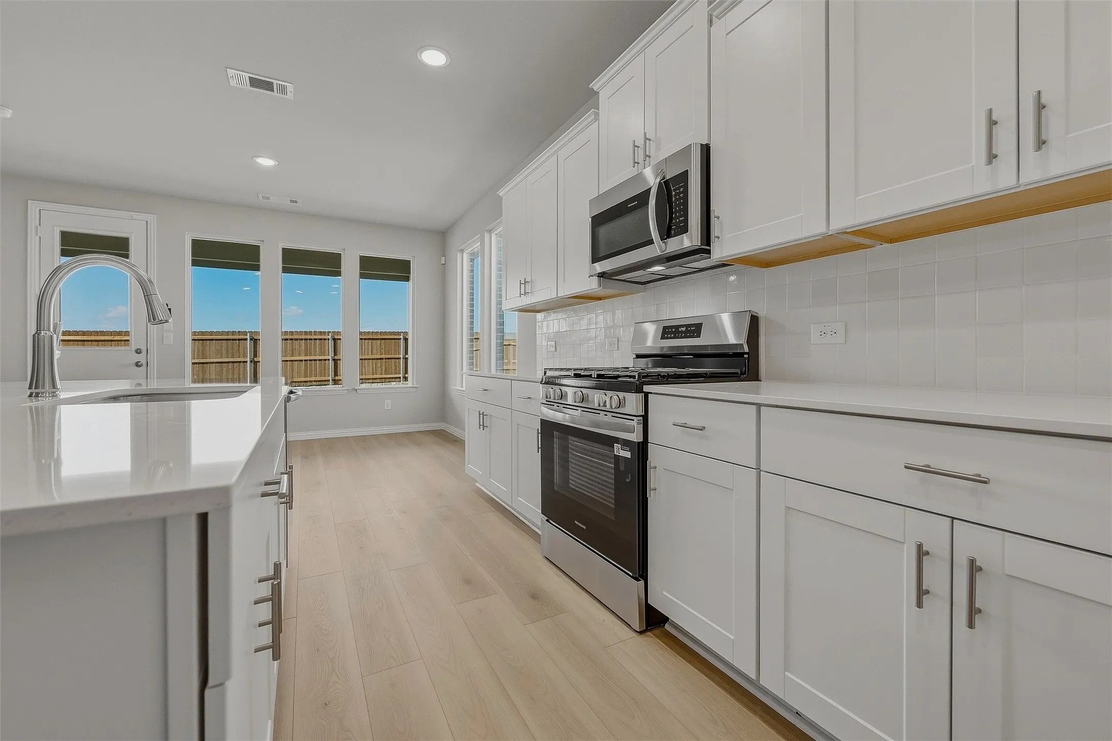 White kitchen cabinetry with stainless steel appliances, light-toned wood-finish flooring, and a large central island with an undermount sink and gooseneck faucet