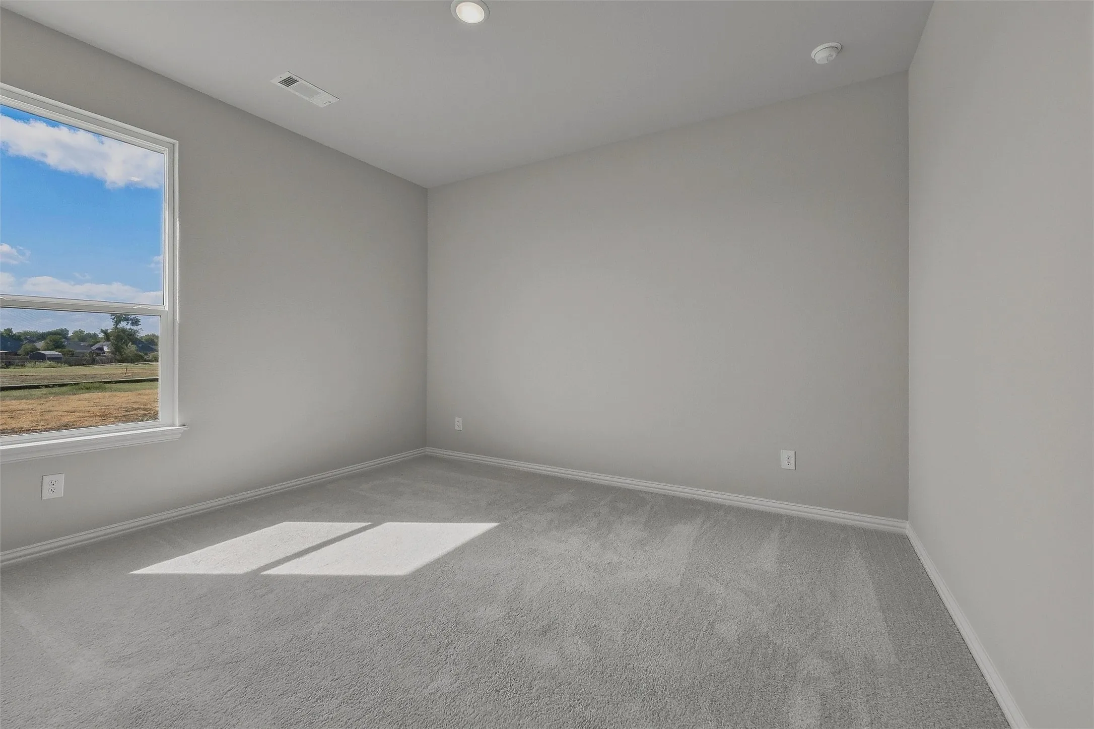 Recessed lighting, light gray wall paint, gray carpet flooring, and a window framing a clear sky