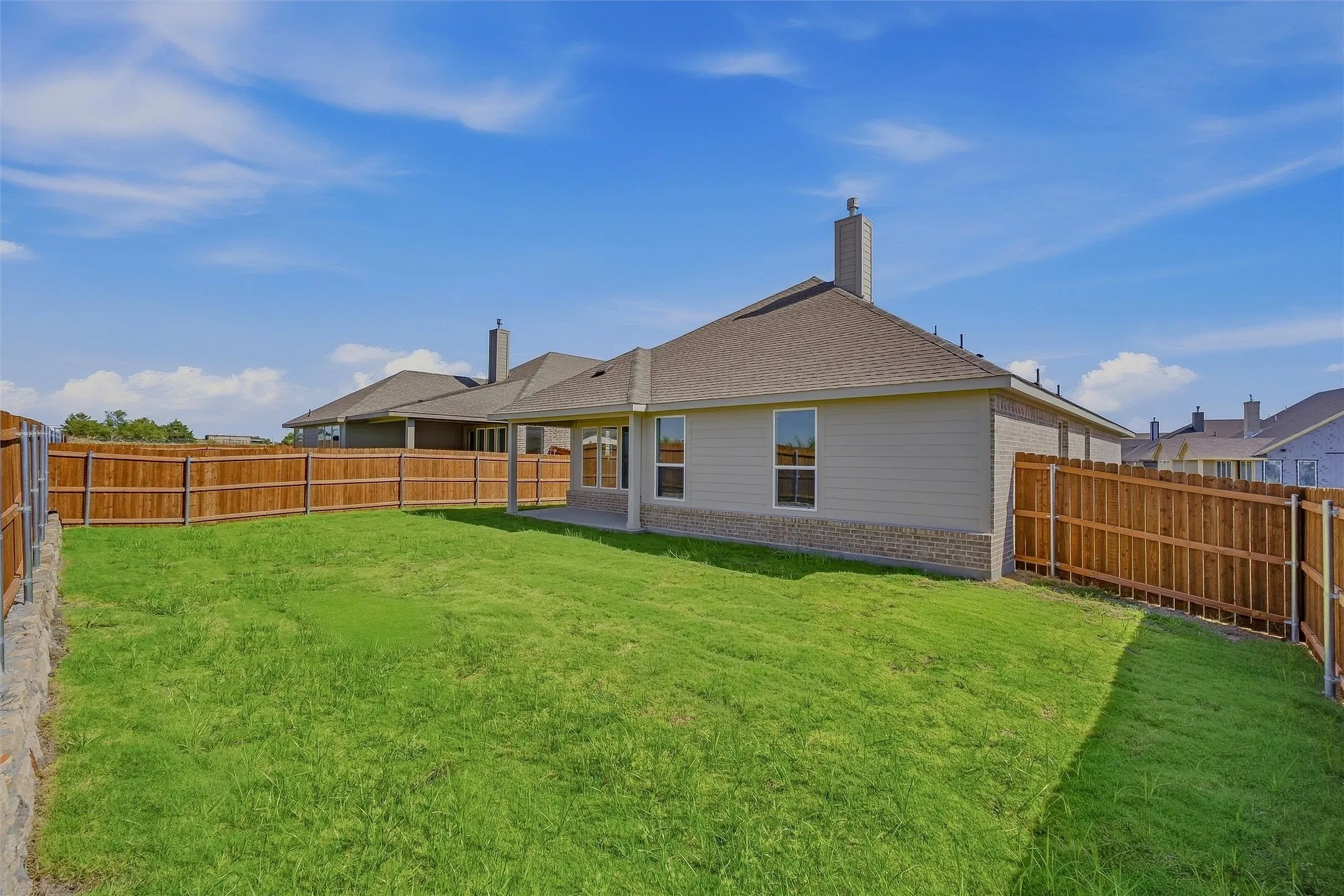 Expansive grassy yard with wood fencing, a covered patio, and a stone and siding exterior