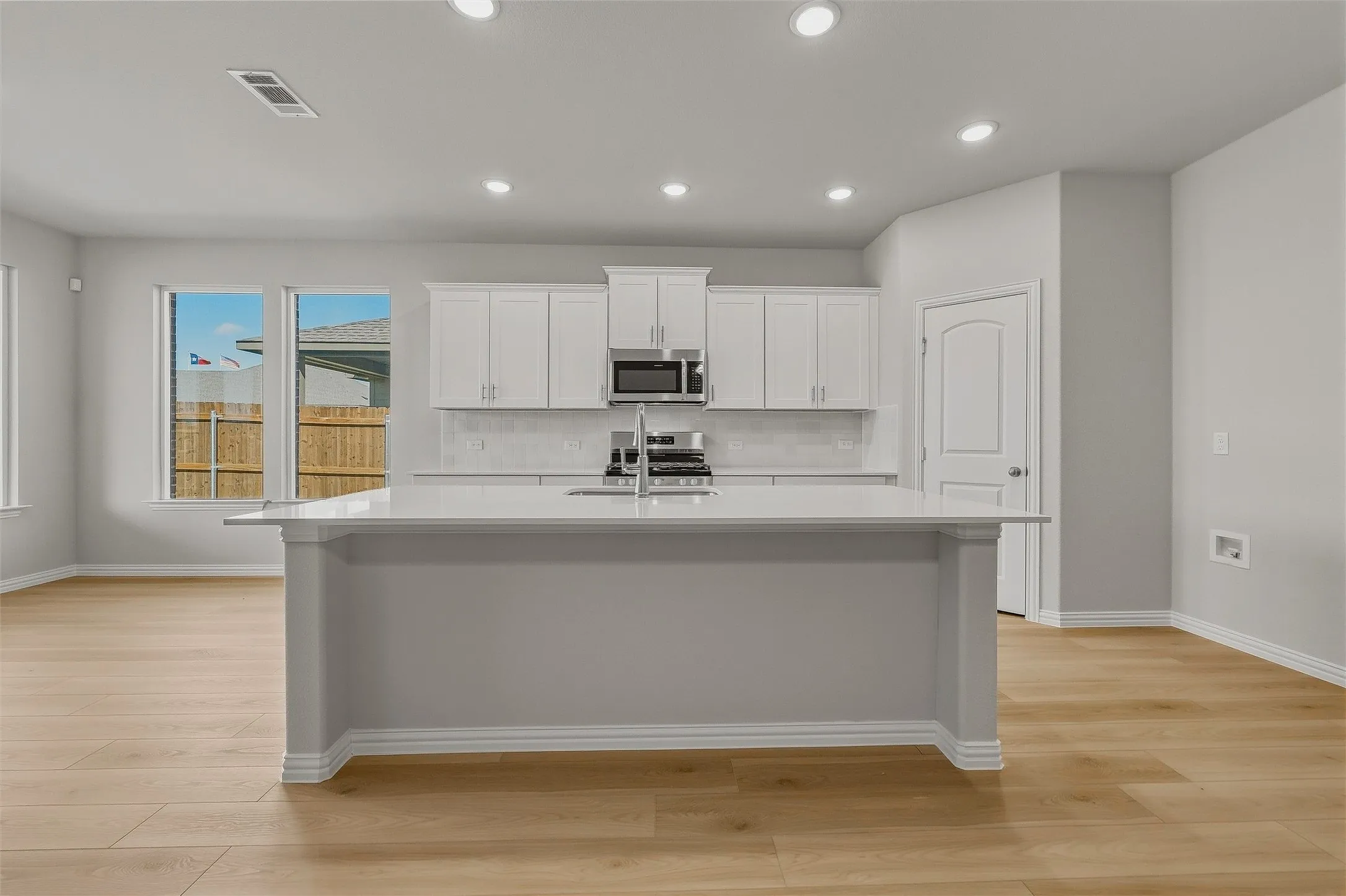 Open-concept kitchen with a large central island, white cabinetry, integrated stainless steel appliances, and light wood-finish flooring throughout