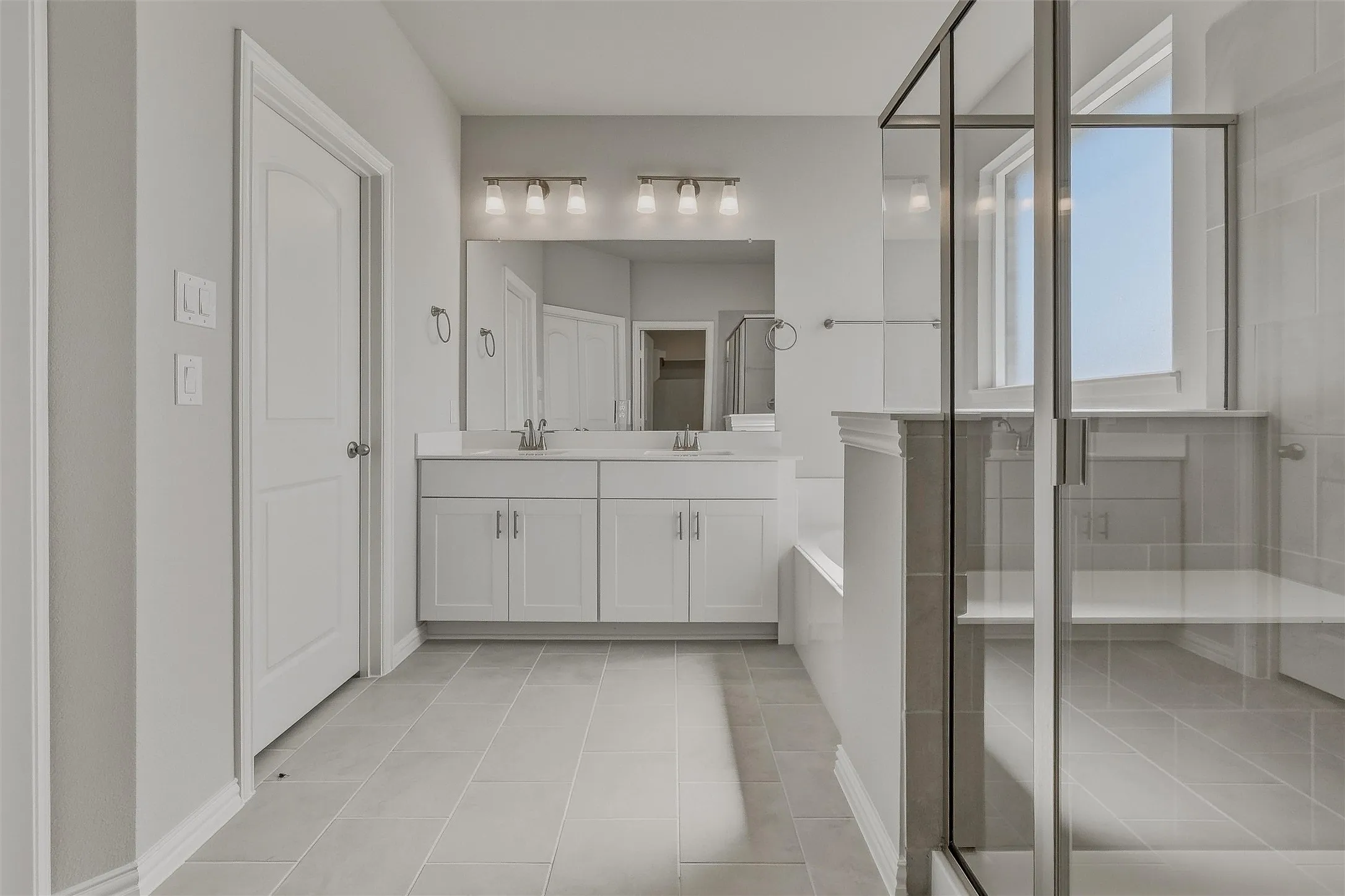 Dual vanity with white cabinetry and chrome hardware, large rectangular mirror, and an adjacent walk-in shower with clear glass enclosure