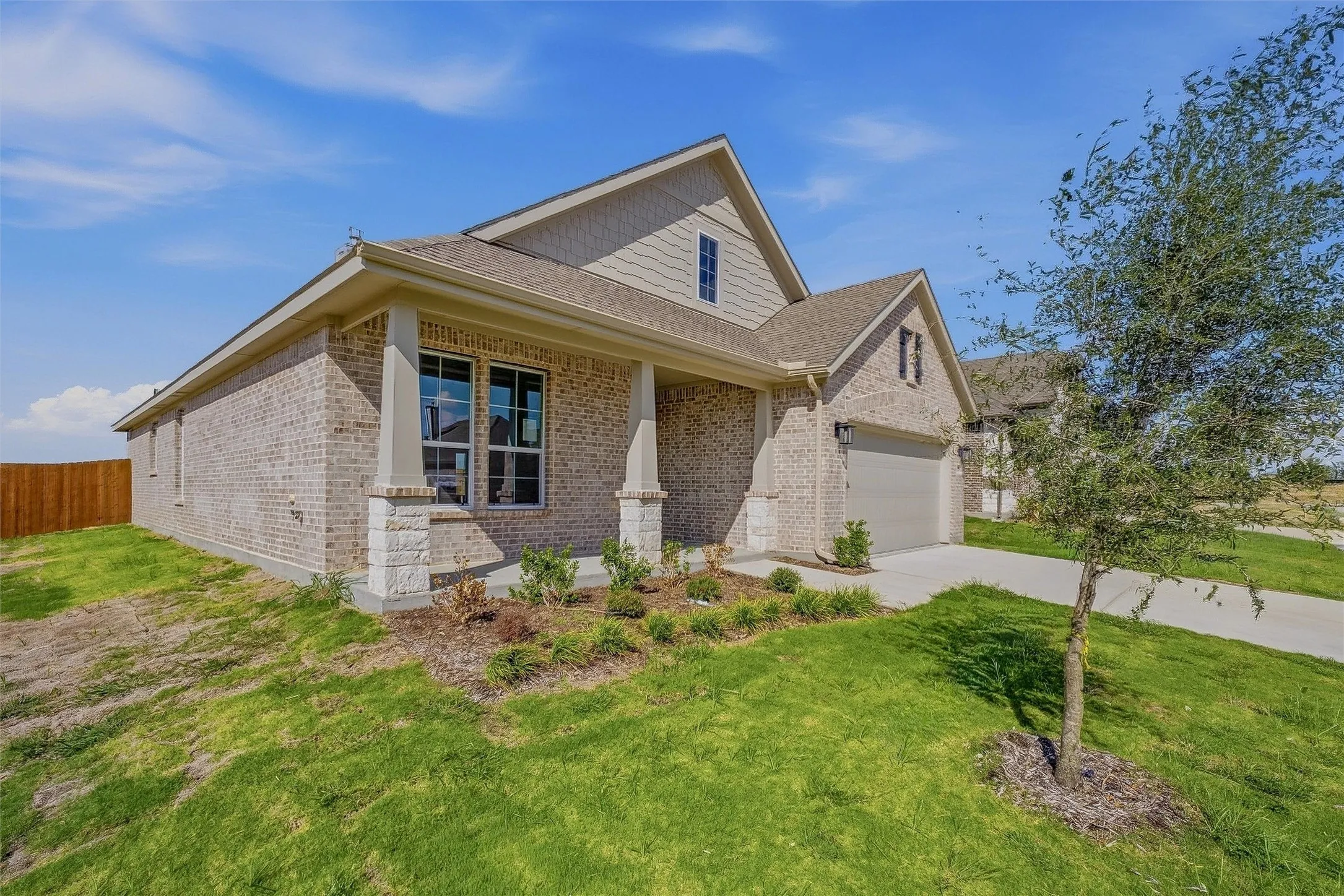 Brick and stone facade, attached garage, covered front entry, concrete driveway, and a fenced backyard
