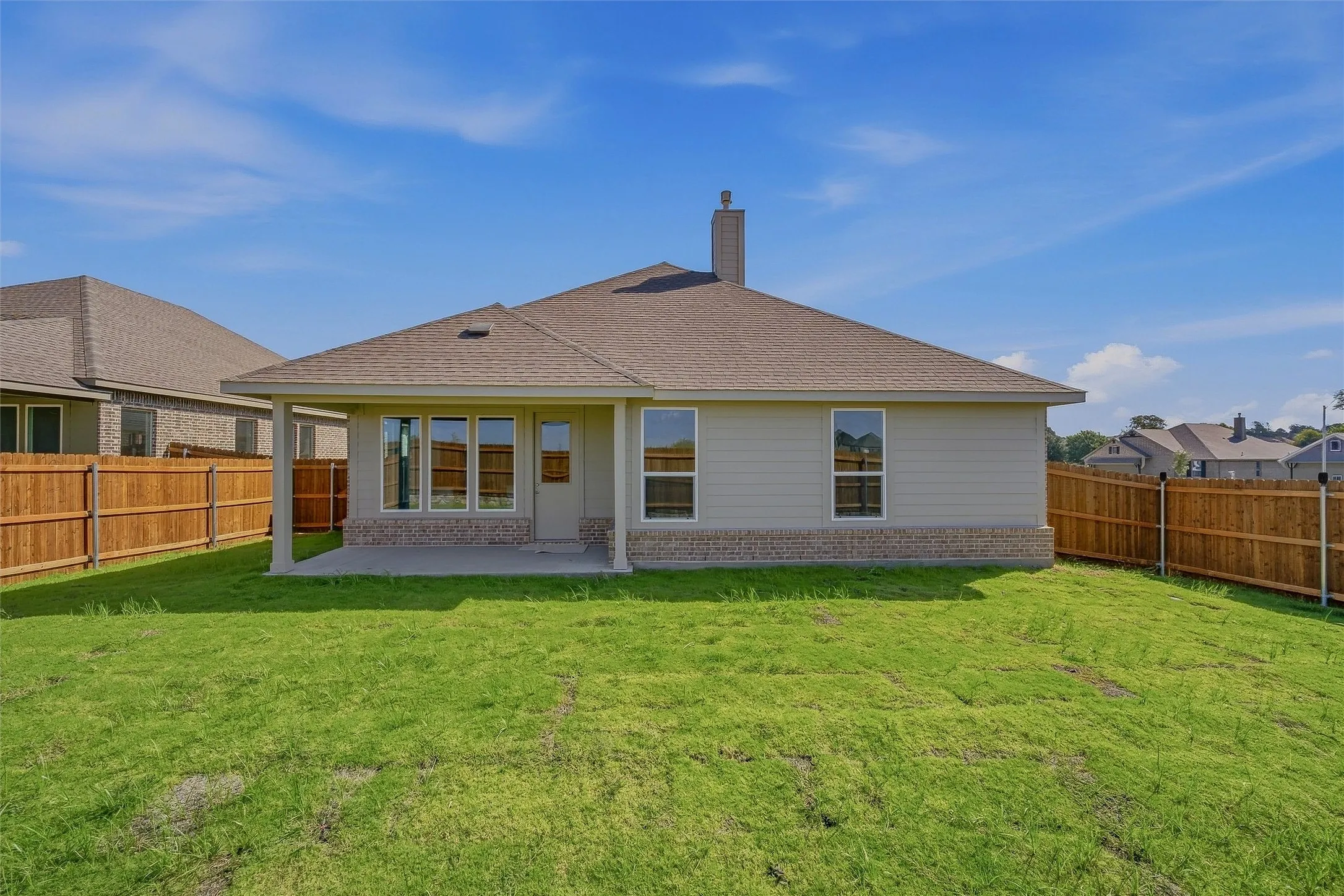 Expansive backyard with a covered patio, wood fencing, and a stucco exterior featuring a stone accent foundation