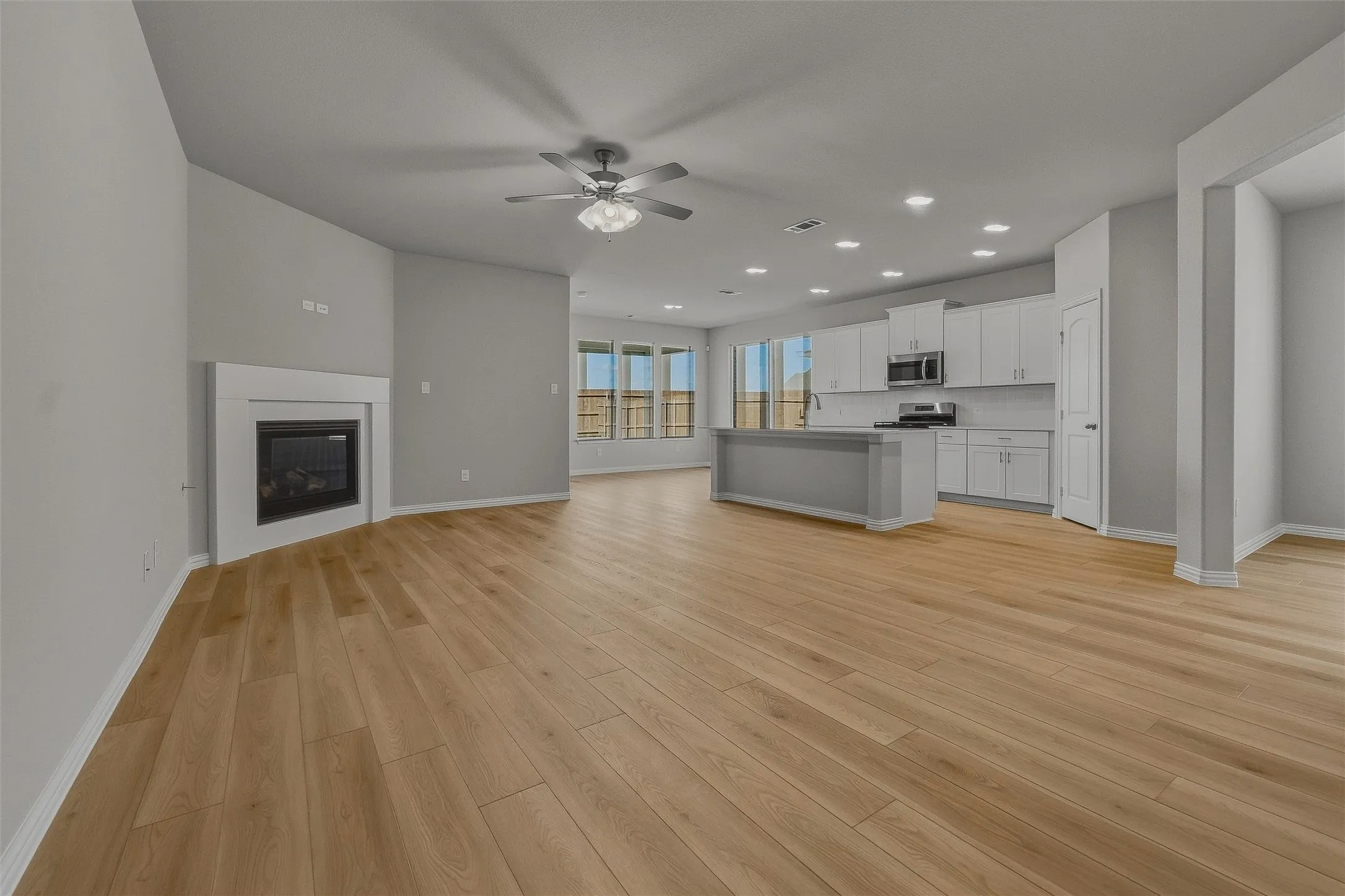 Open-concept living area with wood-finish flooring, a contemporary fireplace, recessed lighting, and a ceiling fan