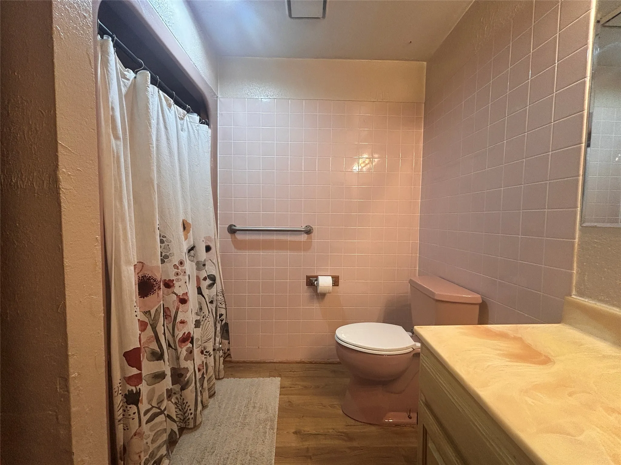 Bathroom featuring pink ceramic wall tiles, a matching pink toilet, and wood-finish flooring
