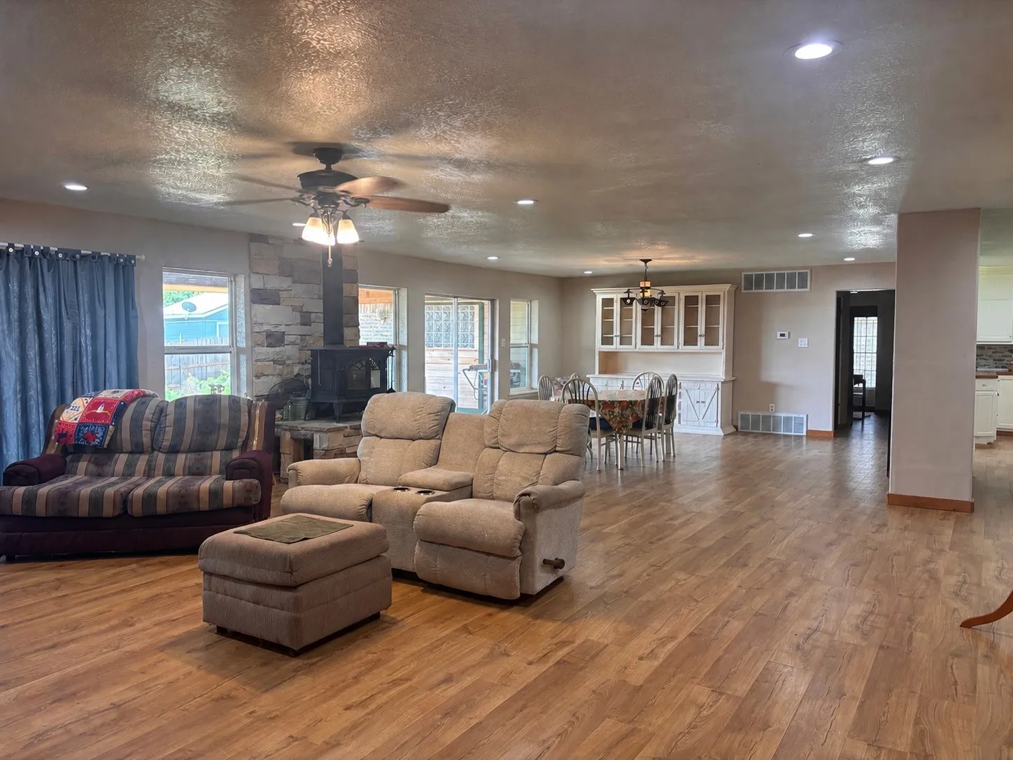 Spacious open-concept living area featuring wood-finish flooring, a stone-faced wood stove, and recessed lighting
(AI Enhanced / Object removal)