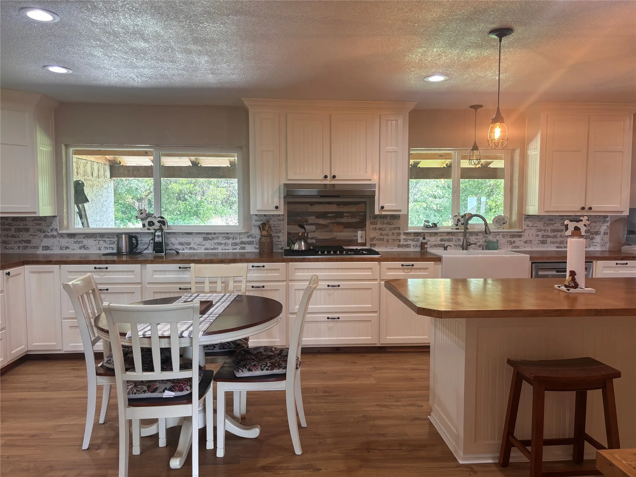 Kitchen featuring white cabinetry, butcher block countertops, white brick-patterned backsplash, wood-finish flooring, and recessed lighting