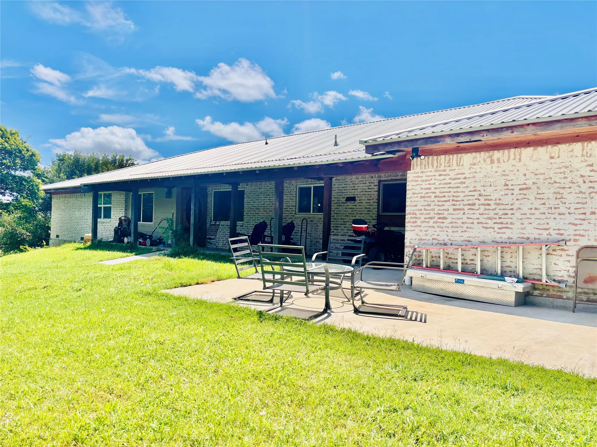 Spacious exterior featuring a durable metal roof, extensive covered patio with exposed wood beams, and a concrete patio