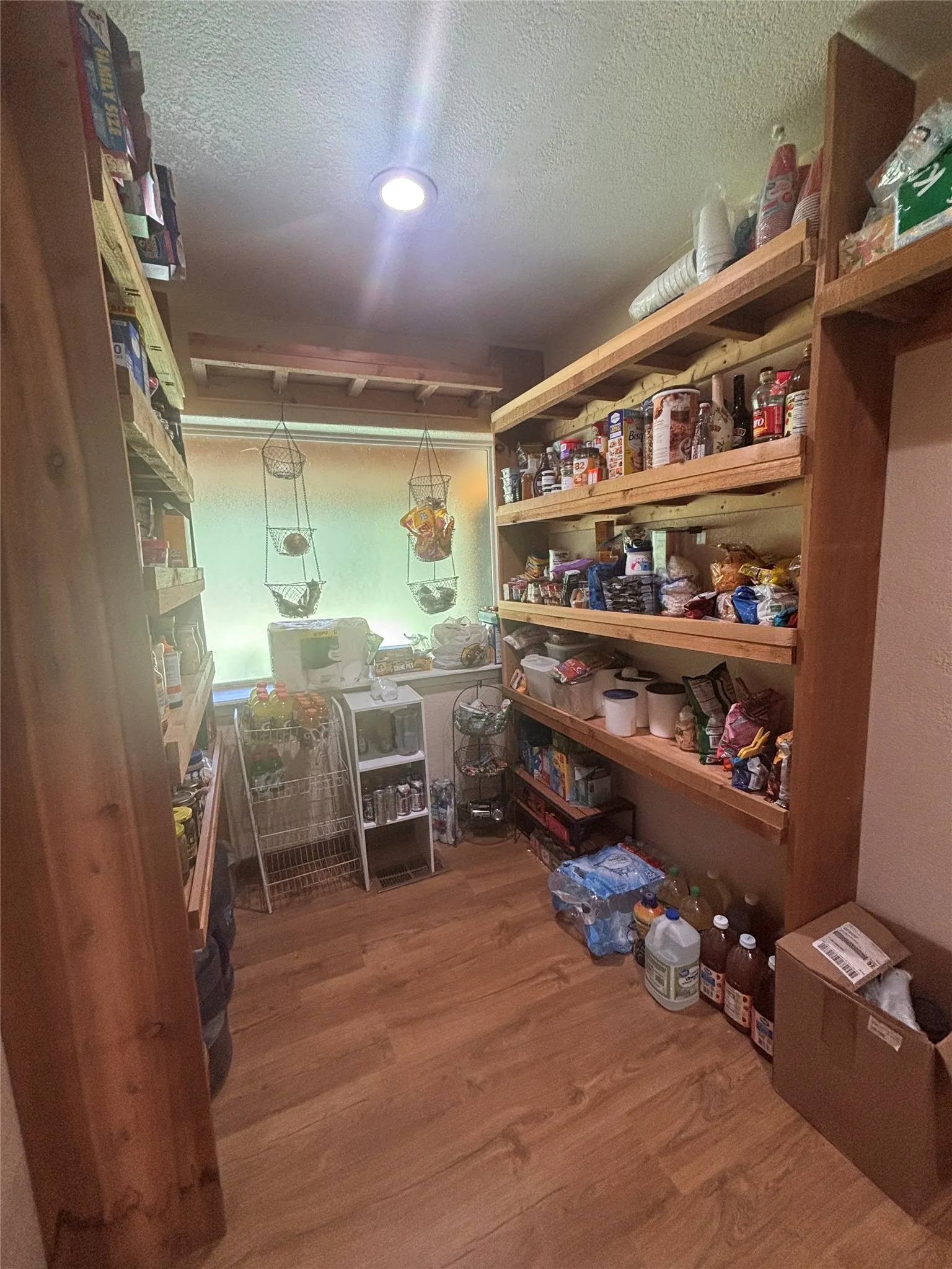 Pantry featuring wood-finish flooring, recessed ceiling lighting, a window, and extensive built-in shelving