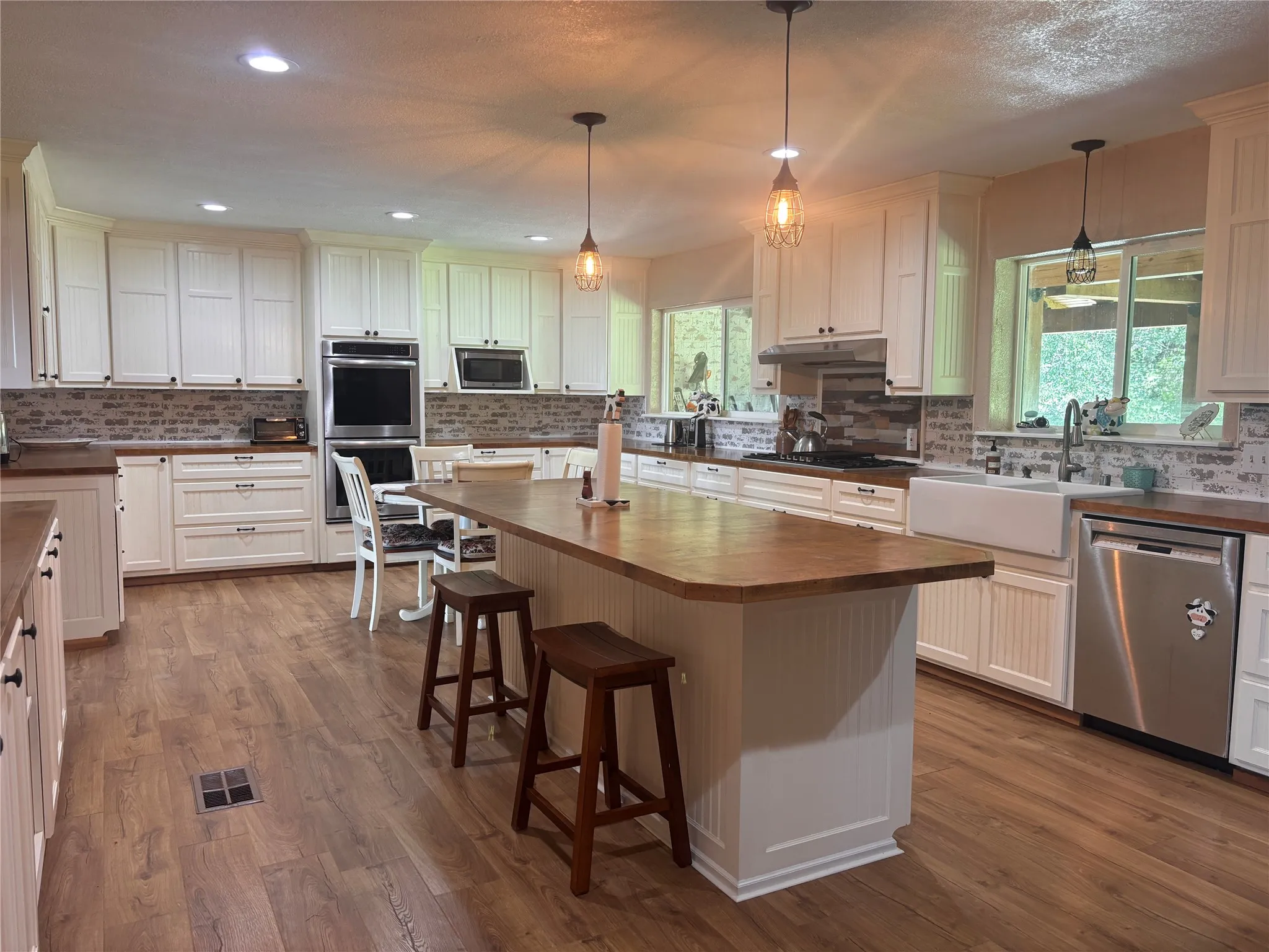 Spacious kitchen featuring extensive white cabinetry, wood-finish countertops, and a large central island with seating