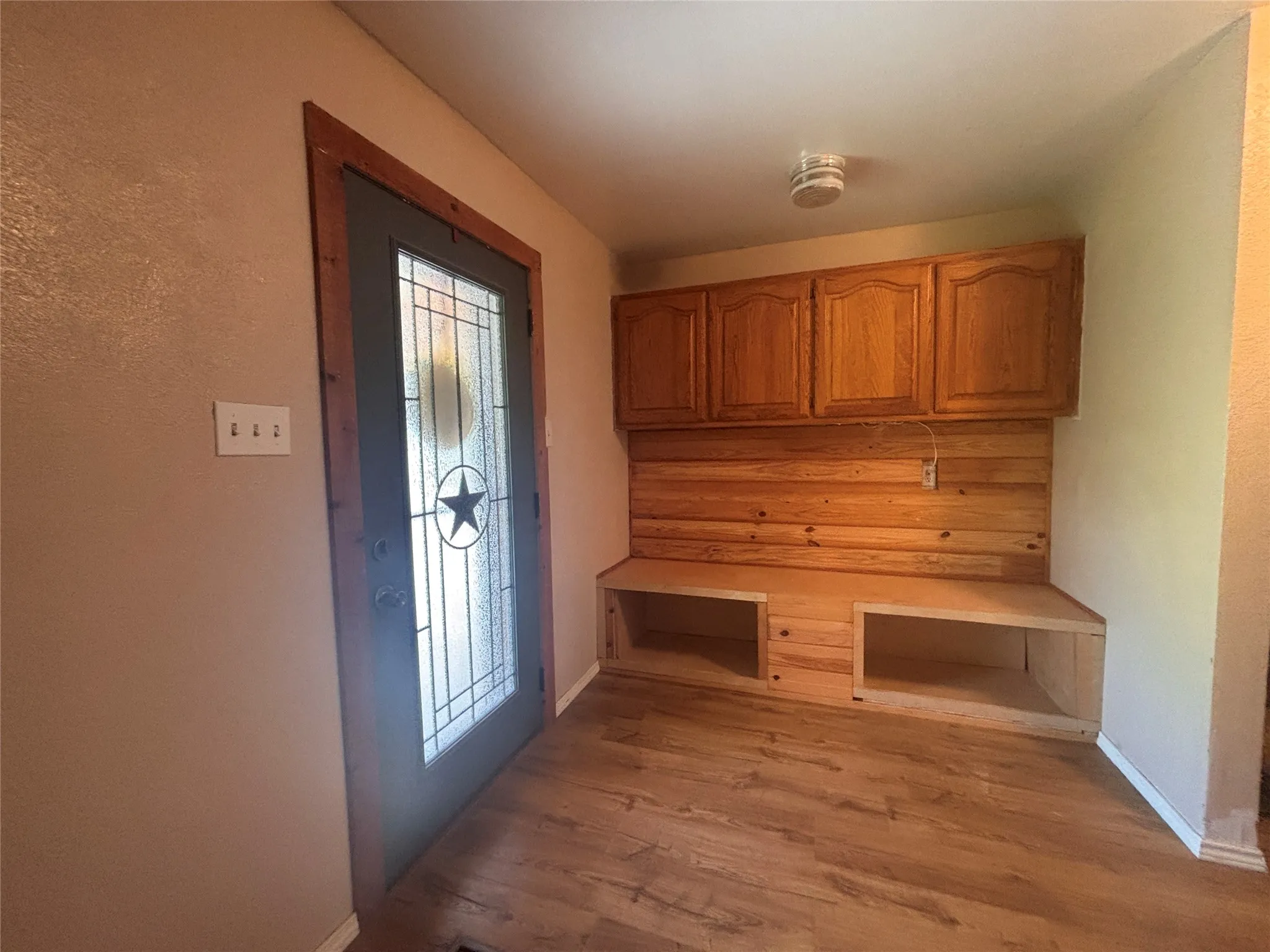Entryway featuring a decorative glass-paneled door, wood-finish flooring, built-in wooden cabinetry, and an integrated bench with open storage compartments