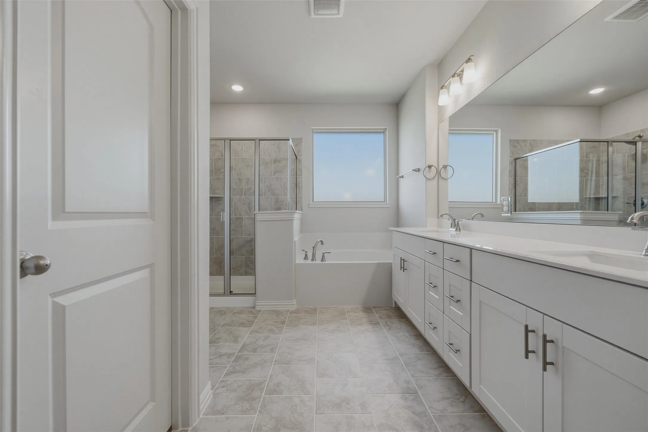 Dual vanity with white cabinetry and integrated sinks, a built-in soaking tub, a separate glass-enclosed shower, and tile flooring