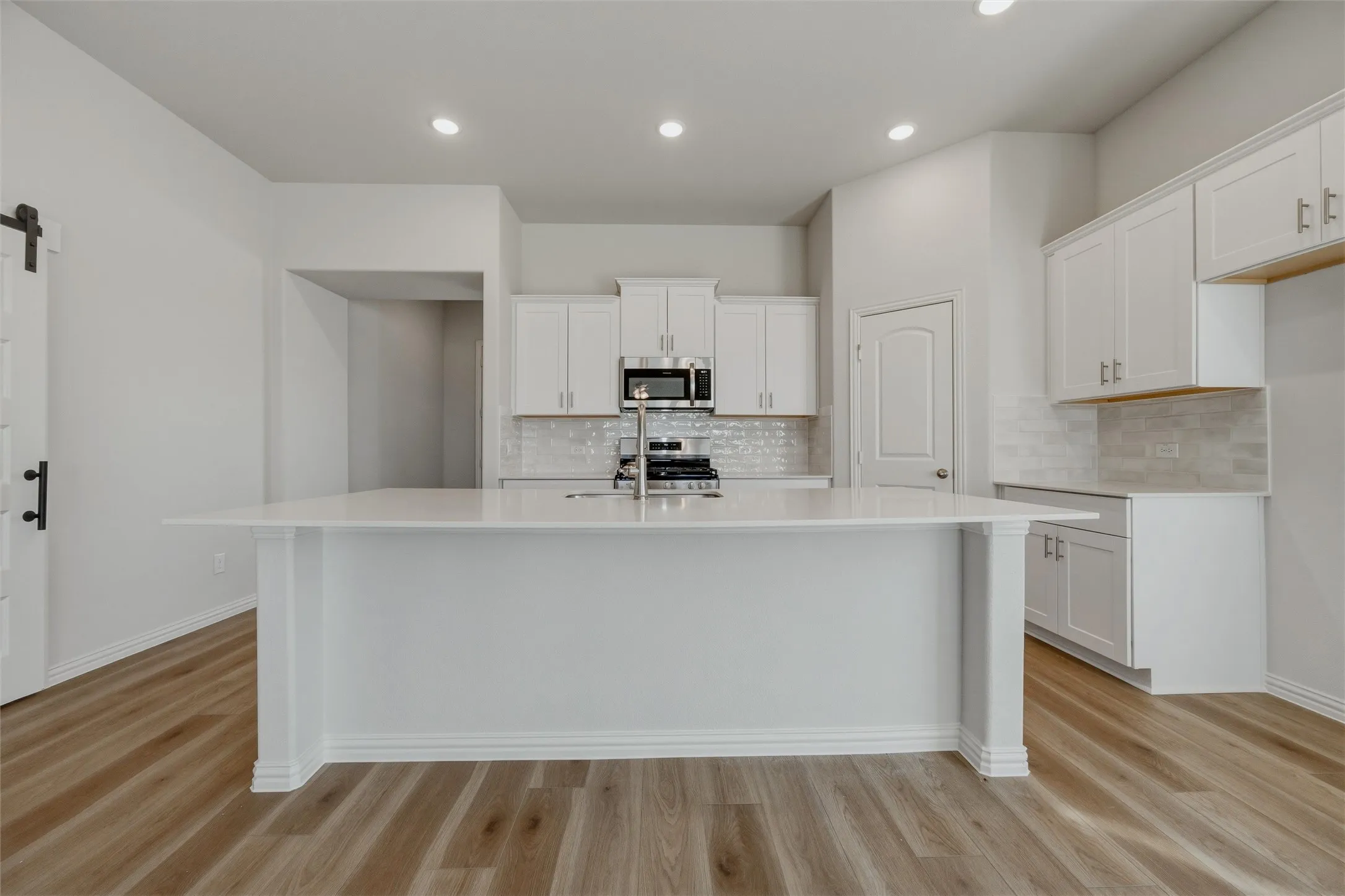 Kitchen featuring a large island, white cabinetry, integrated stainless steel appliances, a tile backsplash, and wood-finish flooring