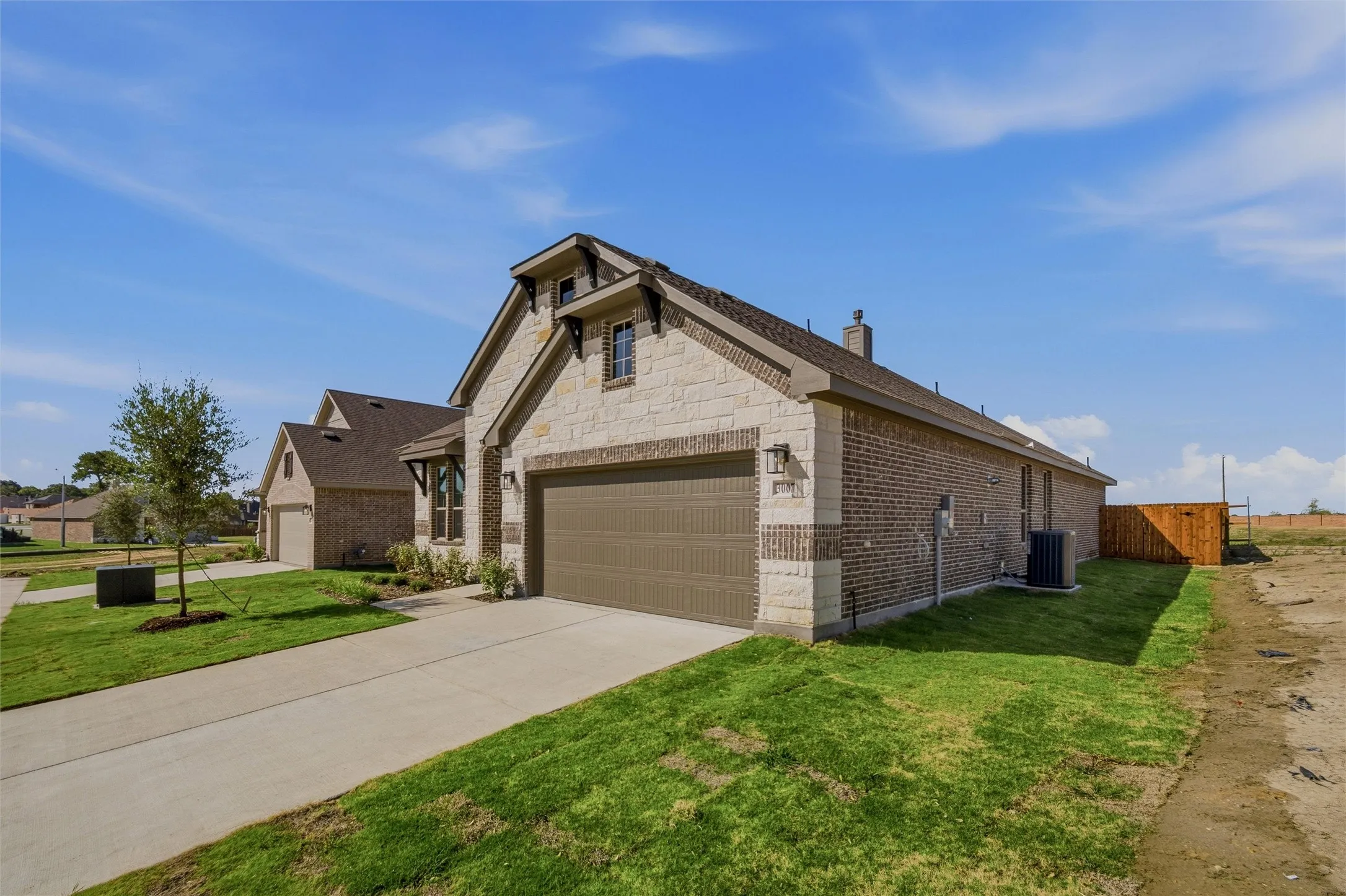 Stone and brick exterior with a two-car garage, concrete driveway, and established landscaping