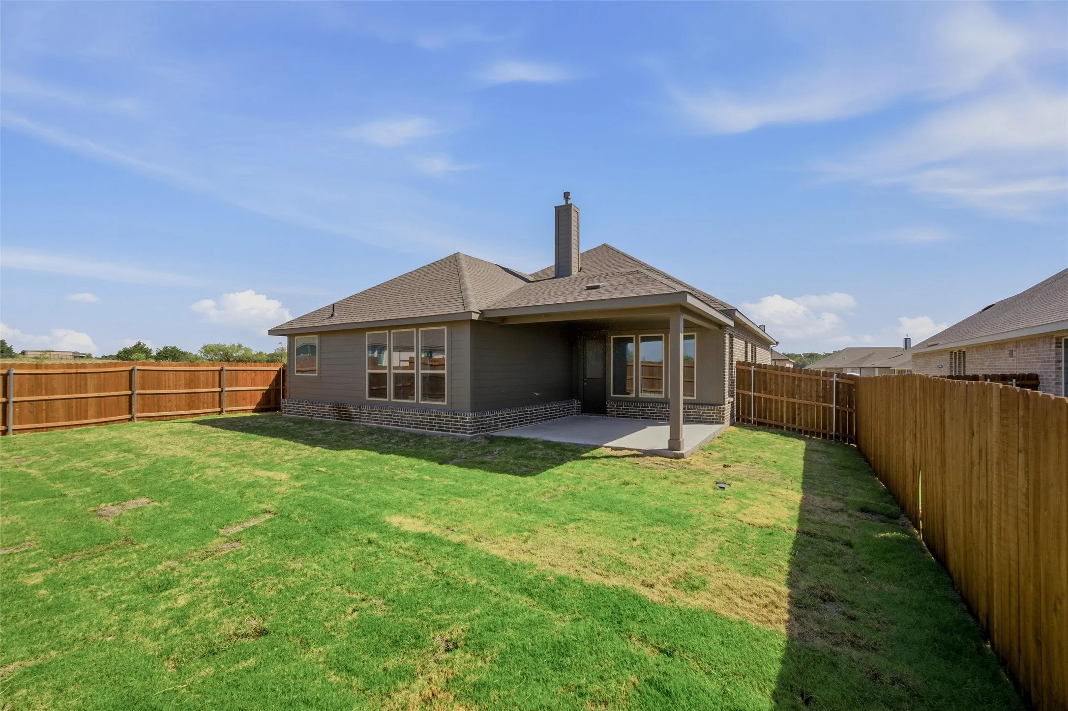 Large fenced backyard with a covered concrete patio, multiple windows, and a chimney feature
