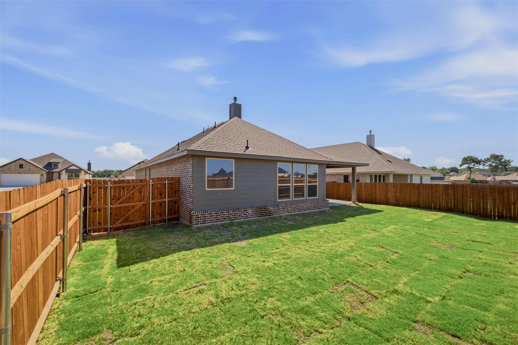 Expansive backyard featuring a newly laid lawn, full privacy fencing, and a covered patio area