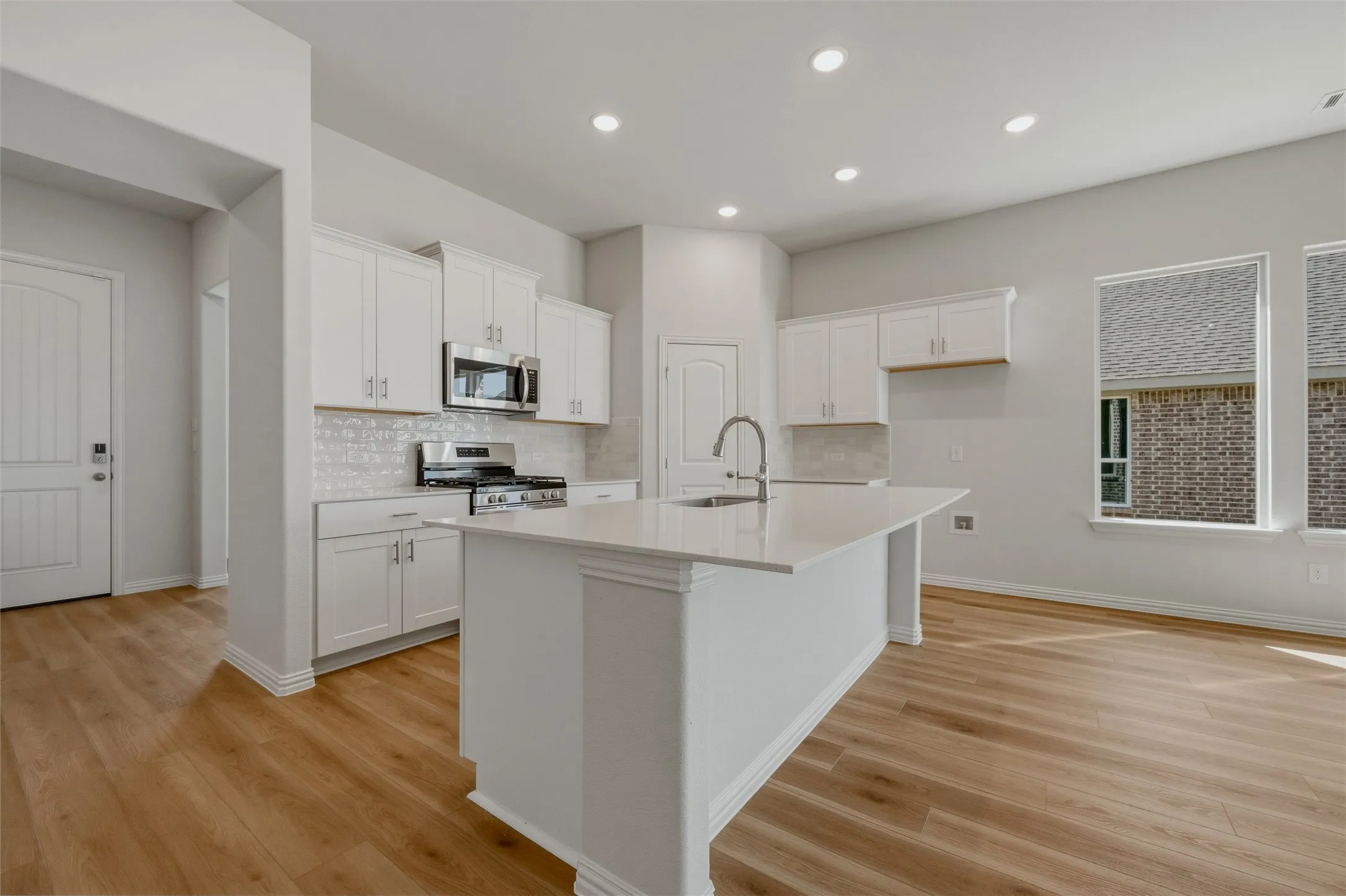 Kitchen featuring a central island with an integrated sink, stainless steel appliances, white cabinetry, and wood-finish flooring