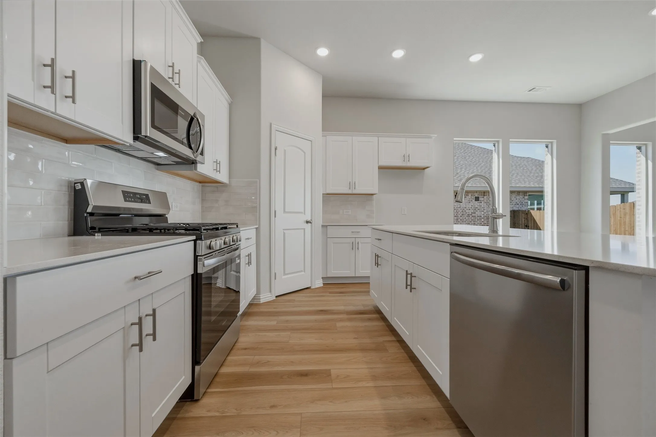 White cabinetry with brushed nickel hardware, stainless steel appliances, light wood-finish flooring, and a kitchen island with an undermount sink