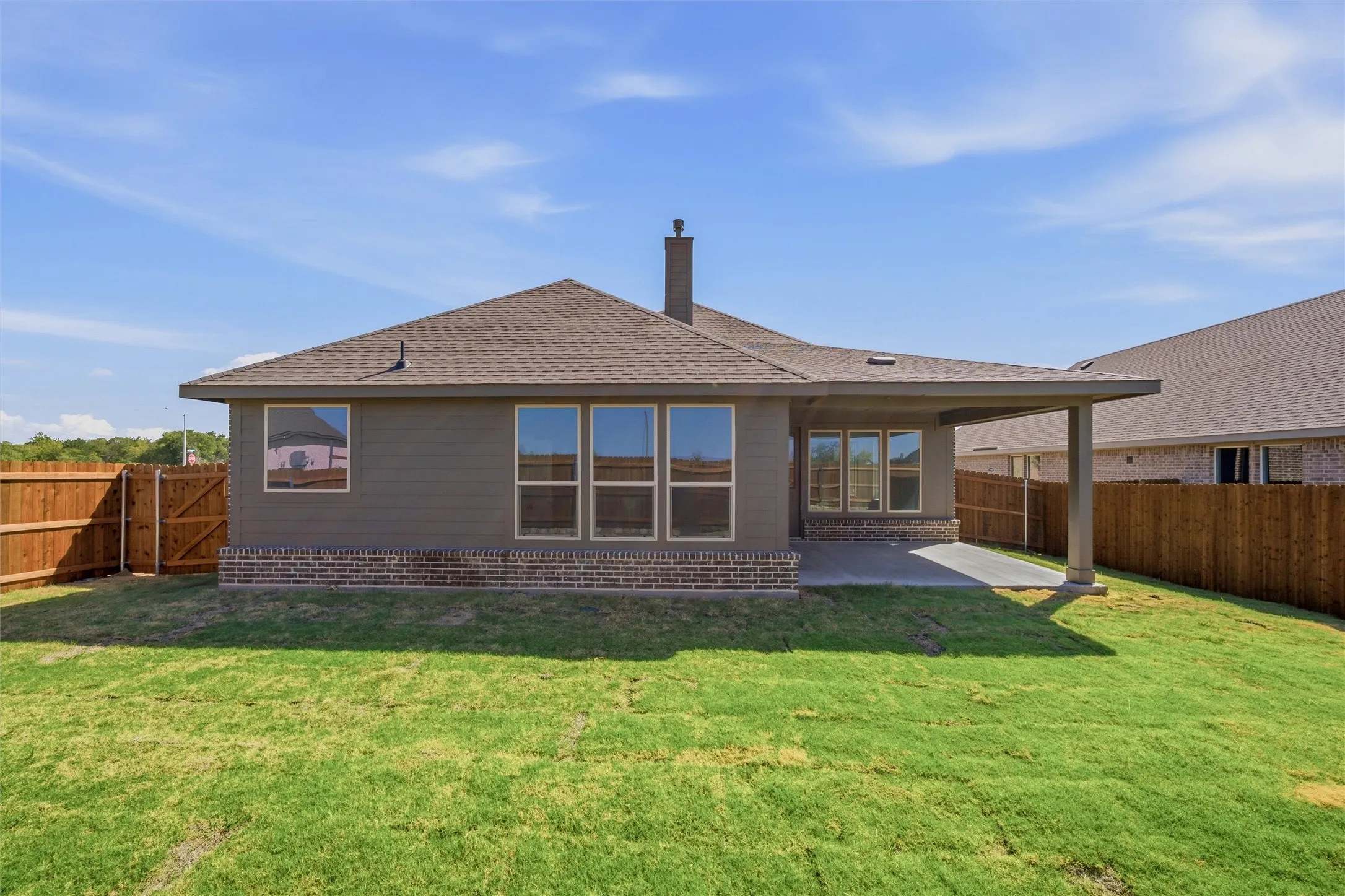 Expansive backyard with a covered patio, brick foundation, multiple windows, and a wood privacy fence