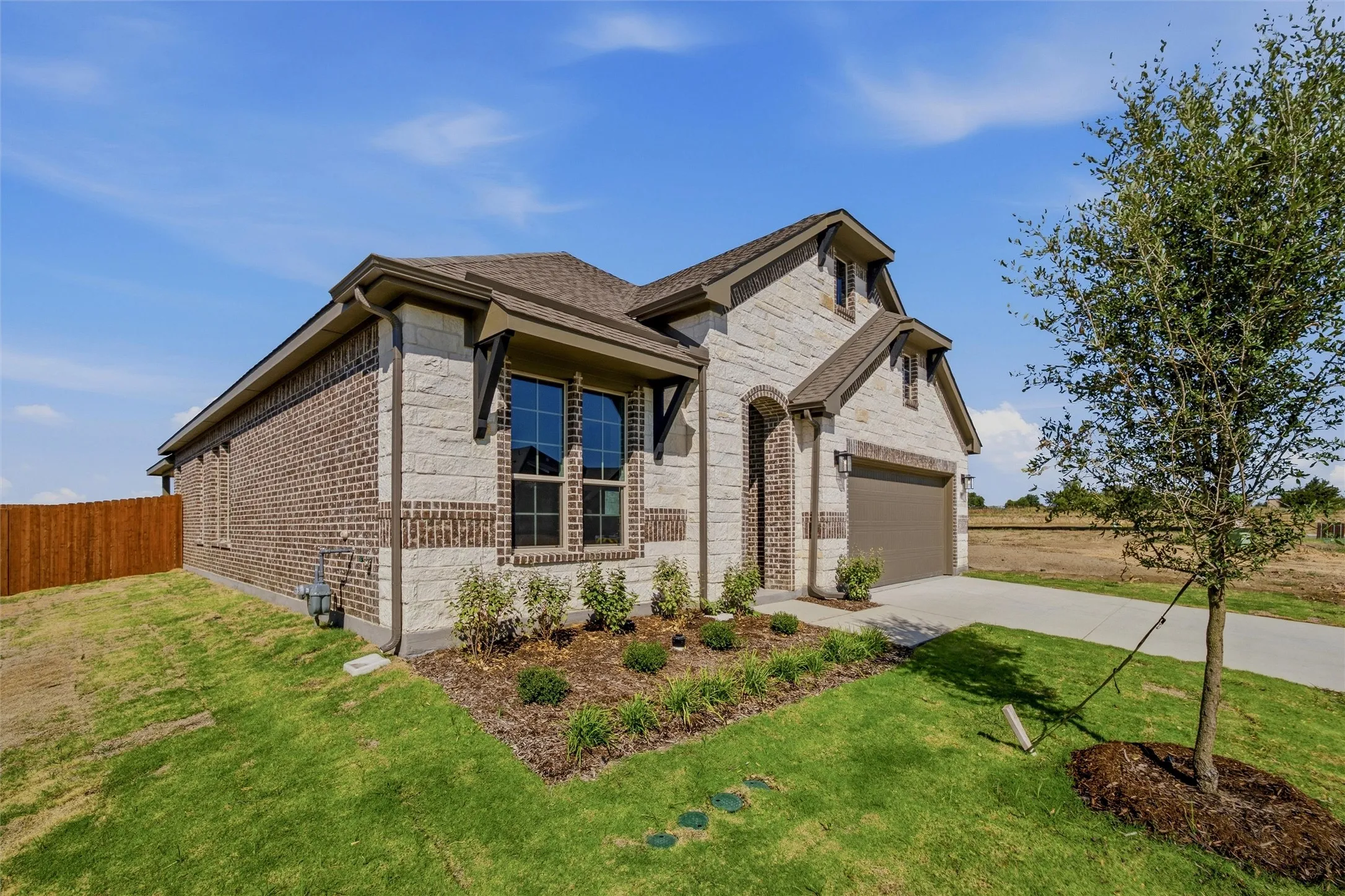 Brick and stone veneer exterior with dark framed windows, attached garage, and a landscaped front yard