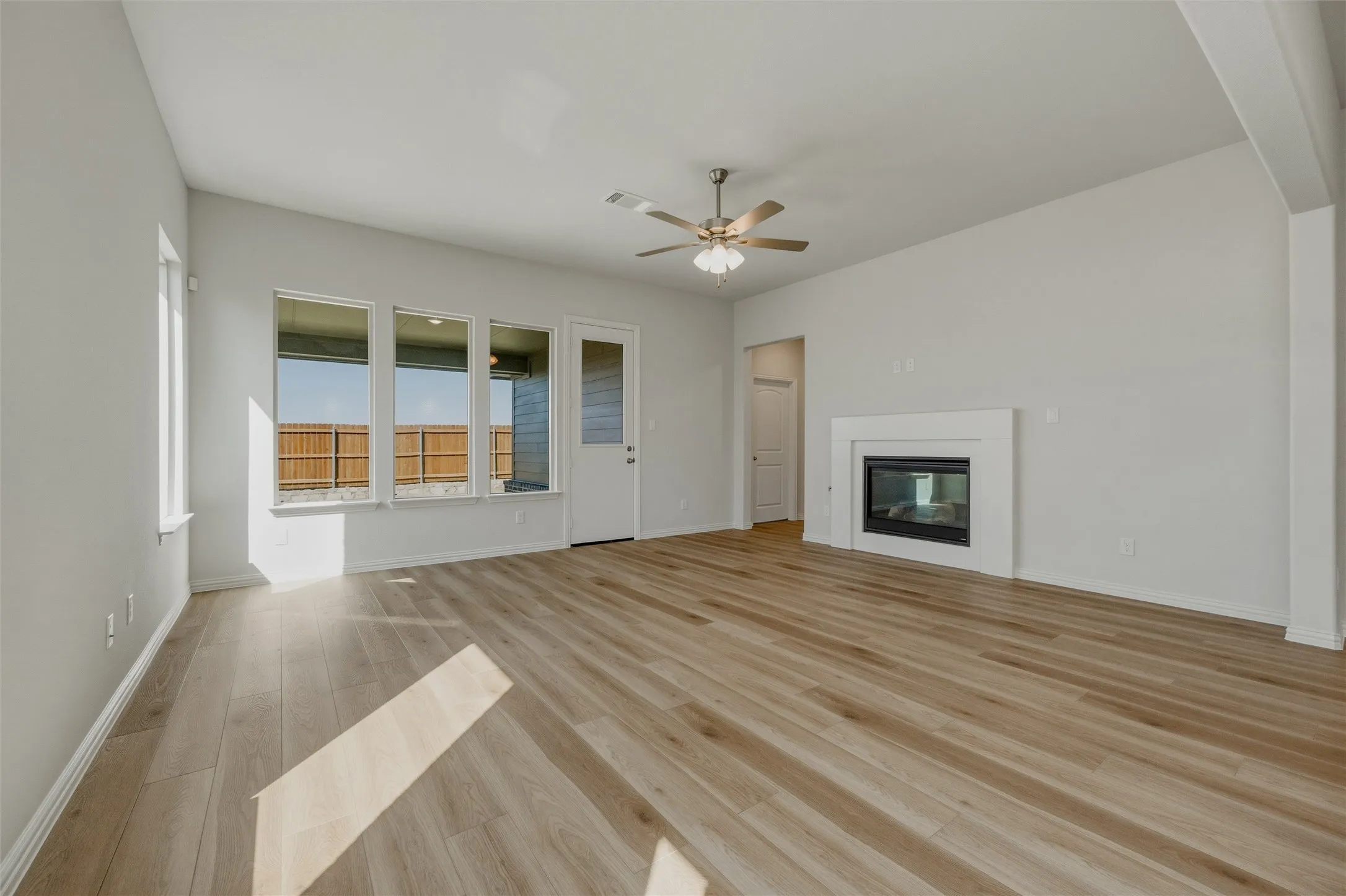 Expansive living area with wood-finish flooring, a contemporary fireplace, and a ceiling fan
