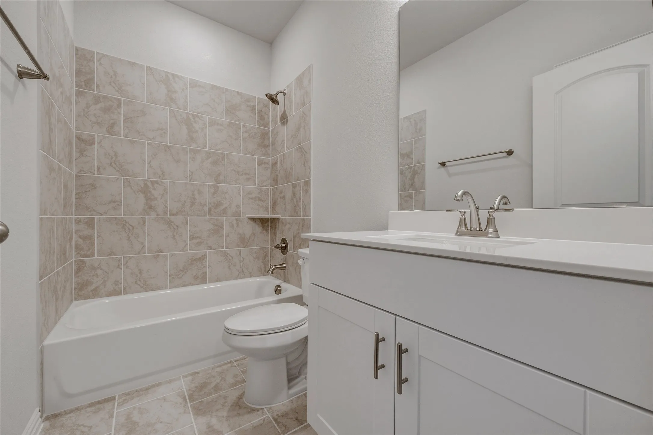 White vanity with white countertop, chrome faucet, tiled flooring, tiled shower surround, and built-in shower niche