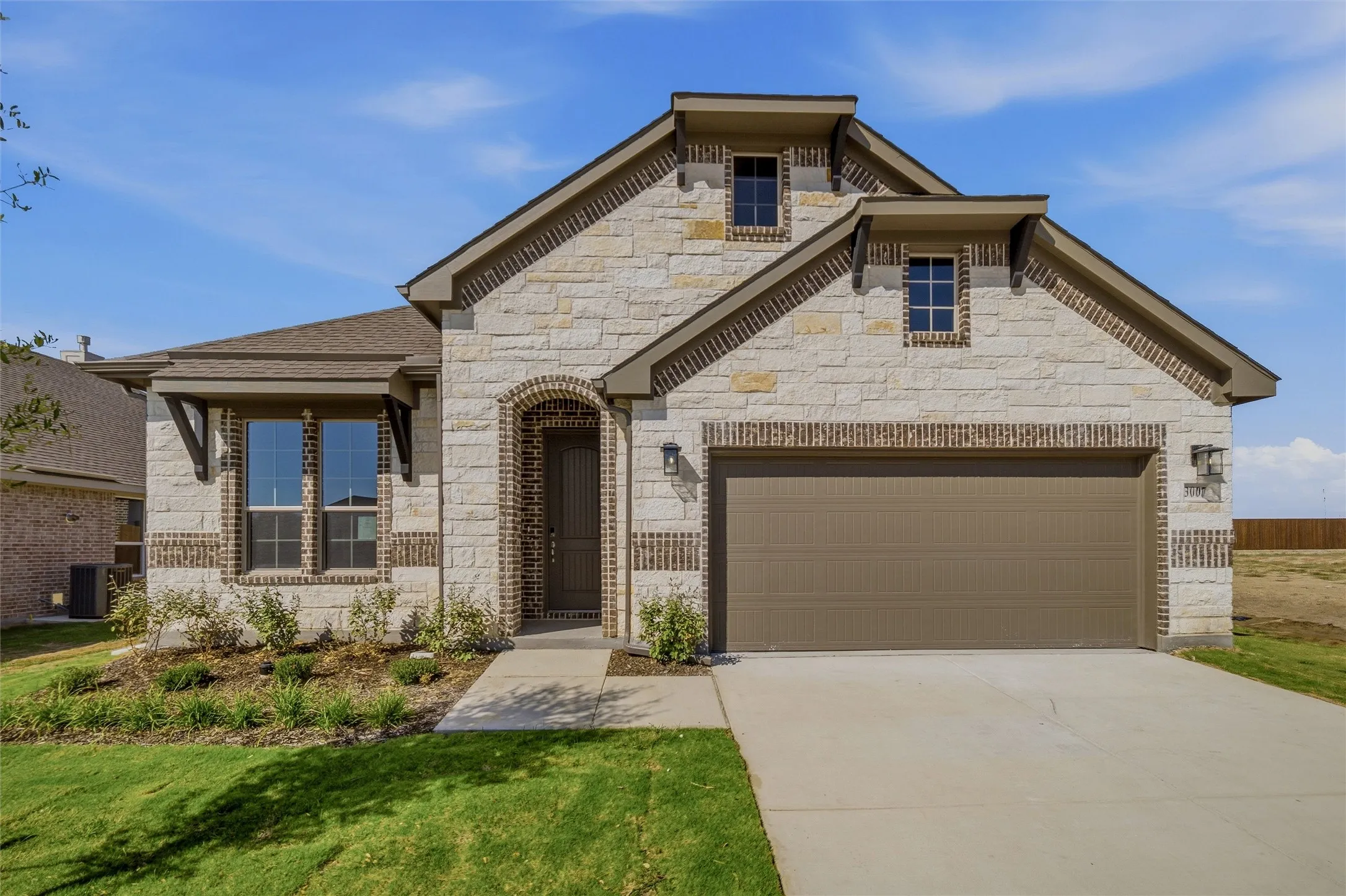 Stone and brick exterior with a two-car garage, arched entry, and decorative dormer windows