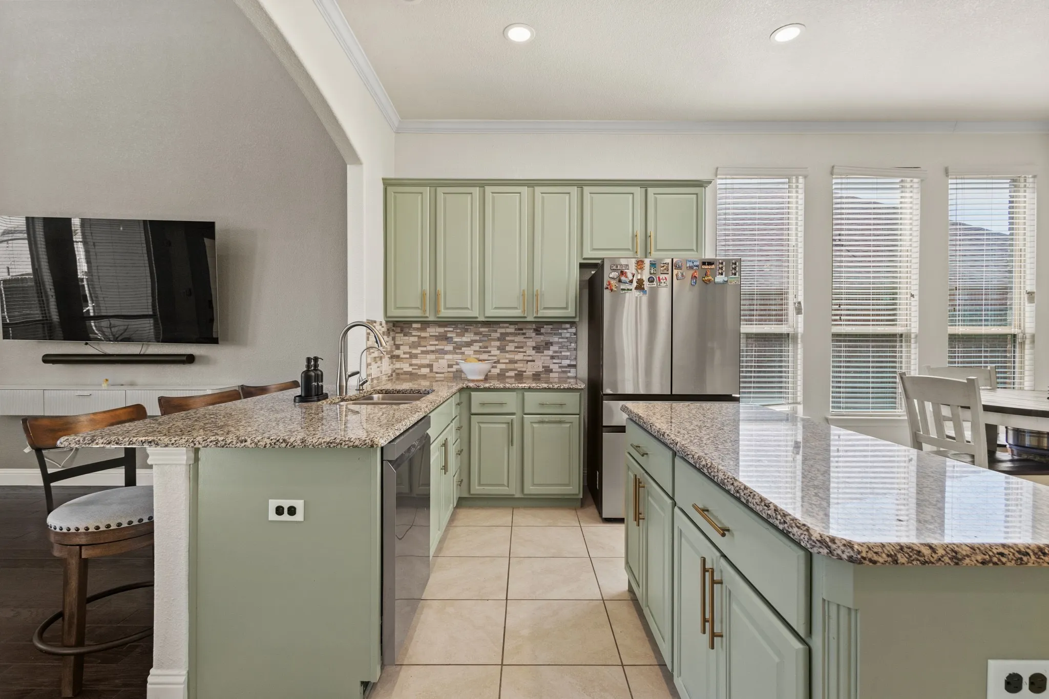 Kitchen with green cabinets, a sink, appliances with stainless steel finishes, ornamental molding, and a peninsula