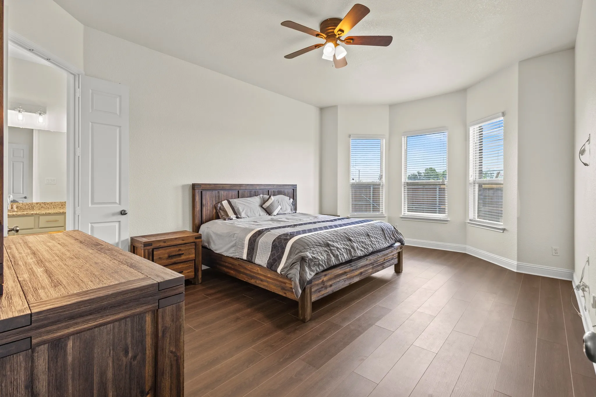 Bedroom featuring dark wood-type flooring, baseboards, a ceiling fan, and ensuite bath