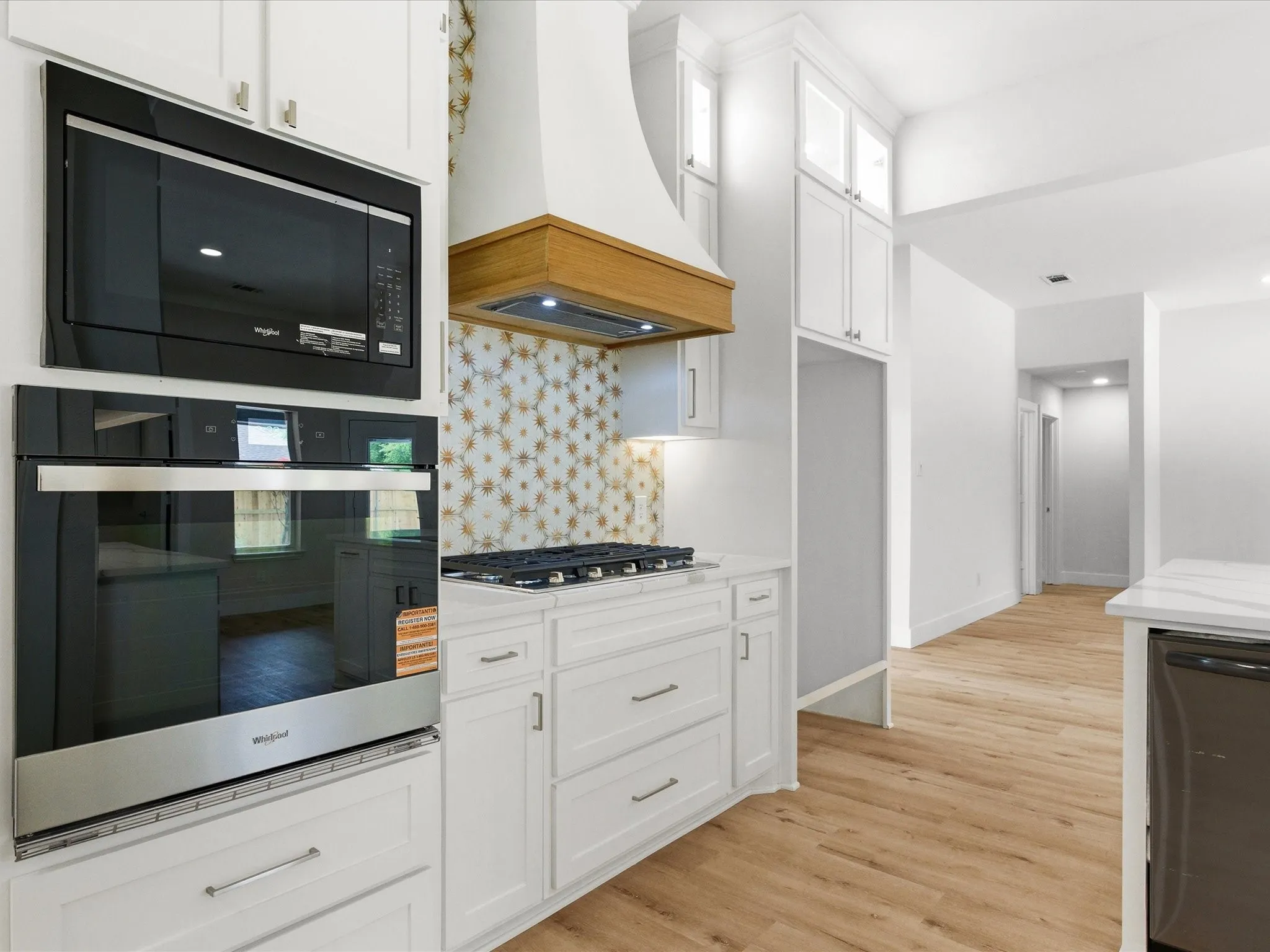 Kitchen with black appliances, white cabinets, light wood-style floors, tasteful backsplash, and light stone countertops