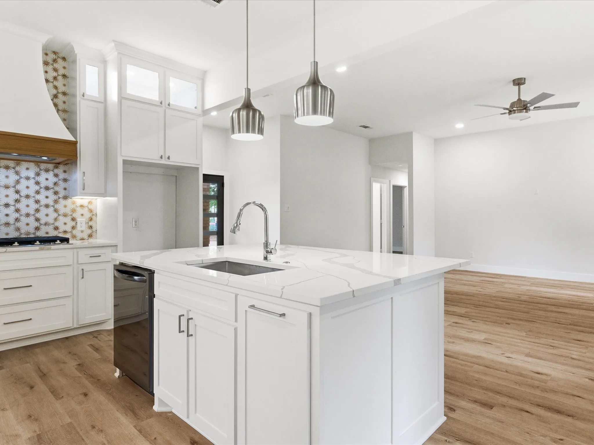 Kitchen with white cabinetry, light stone countertops, an island with sink, and ceiling fan