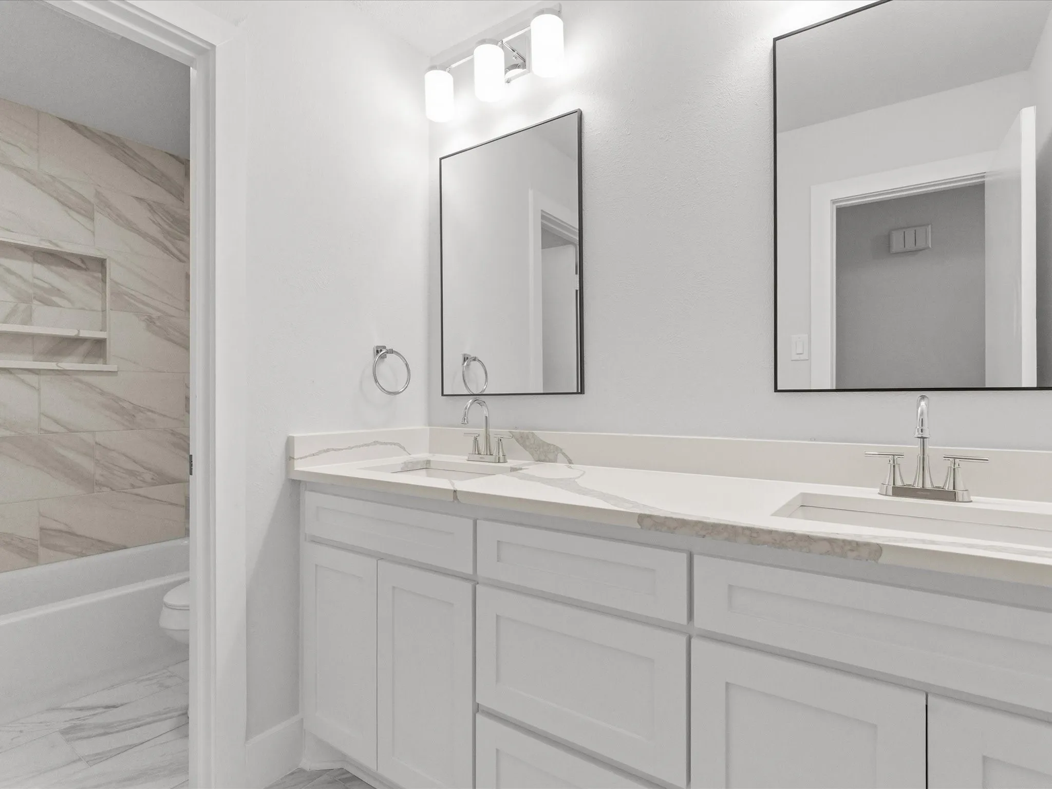 Full bath featuring double vanity, light marble finish floors, and washtub / shower combination