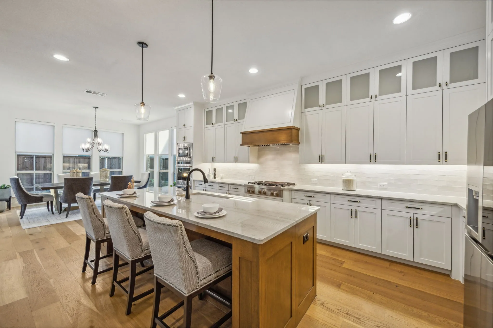 Kitchen featuring custom exhaust hood, a kitchen island with sink, white cabinets, hanging light fixtures, and light stone counters