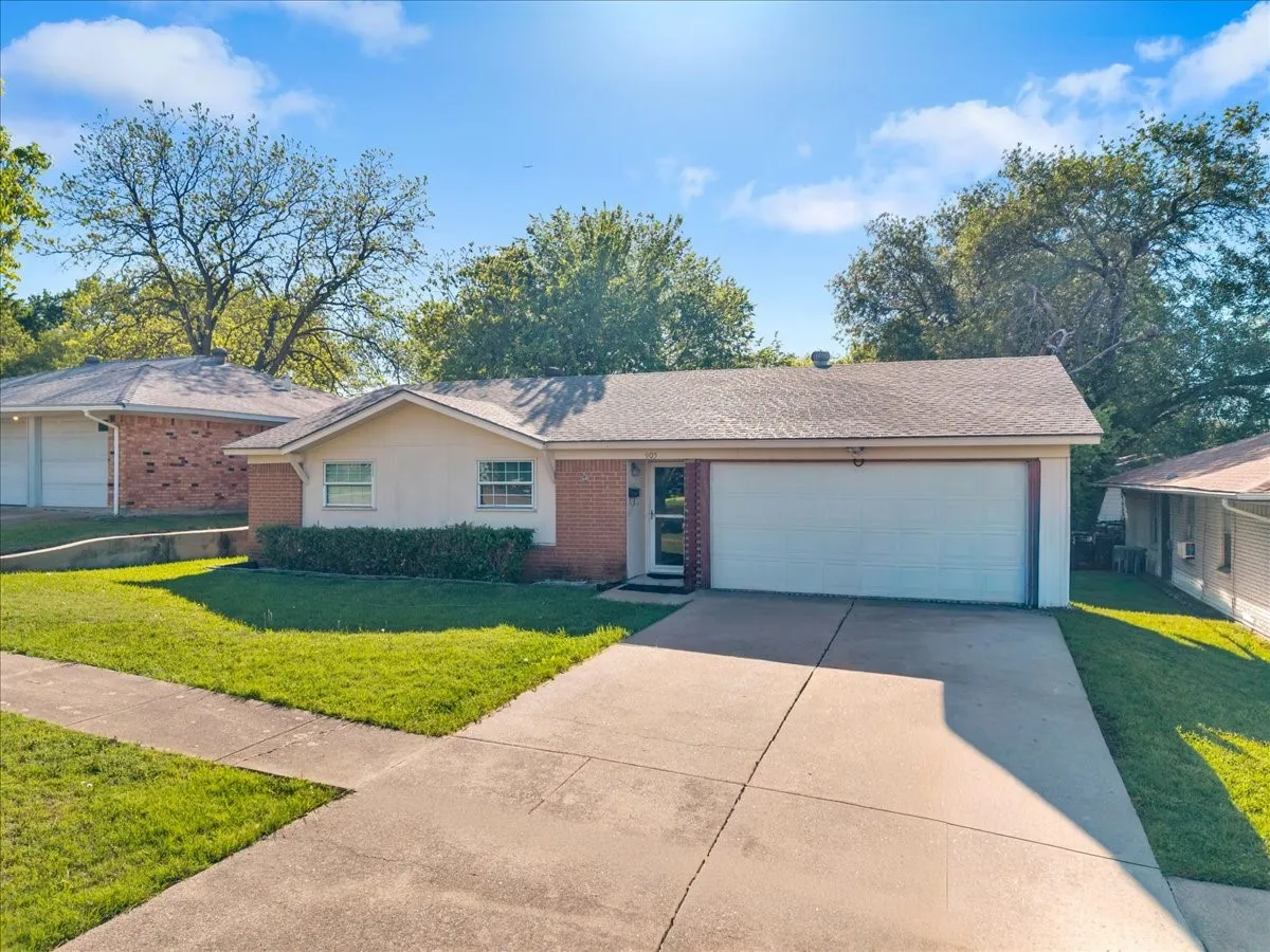 Single story home with brick siding, a garage, a front yard, driveway, and roof with shingles