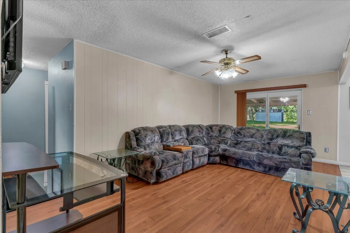 Living area with hardwood / wood-style floors, a textured ceiling, a ceiling fan, and wooden walls