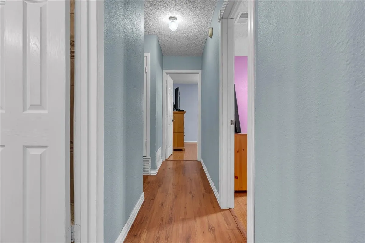Hallway with light wood-type flooring, a textured ceiling, and a textured wall