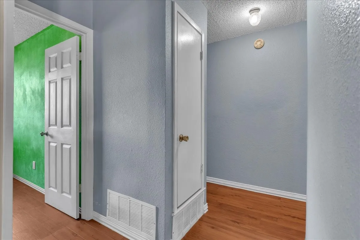 Hall featuring a textured ceiling, a textured wall, and light wood-type flooring