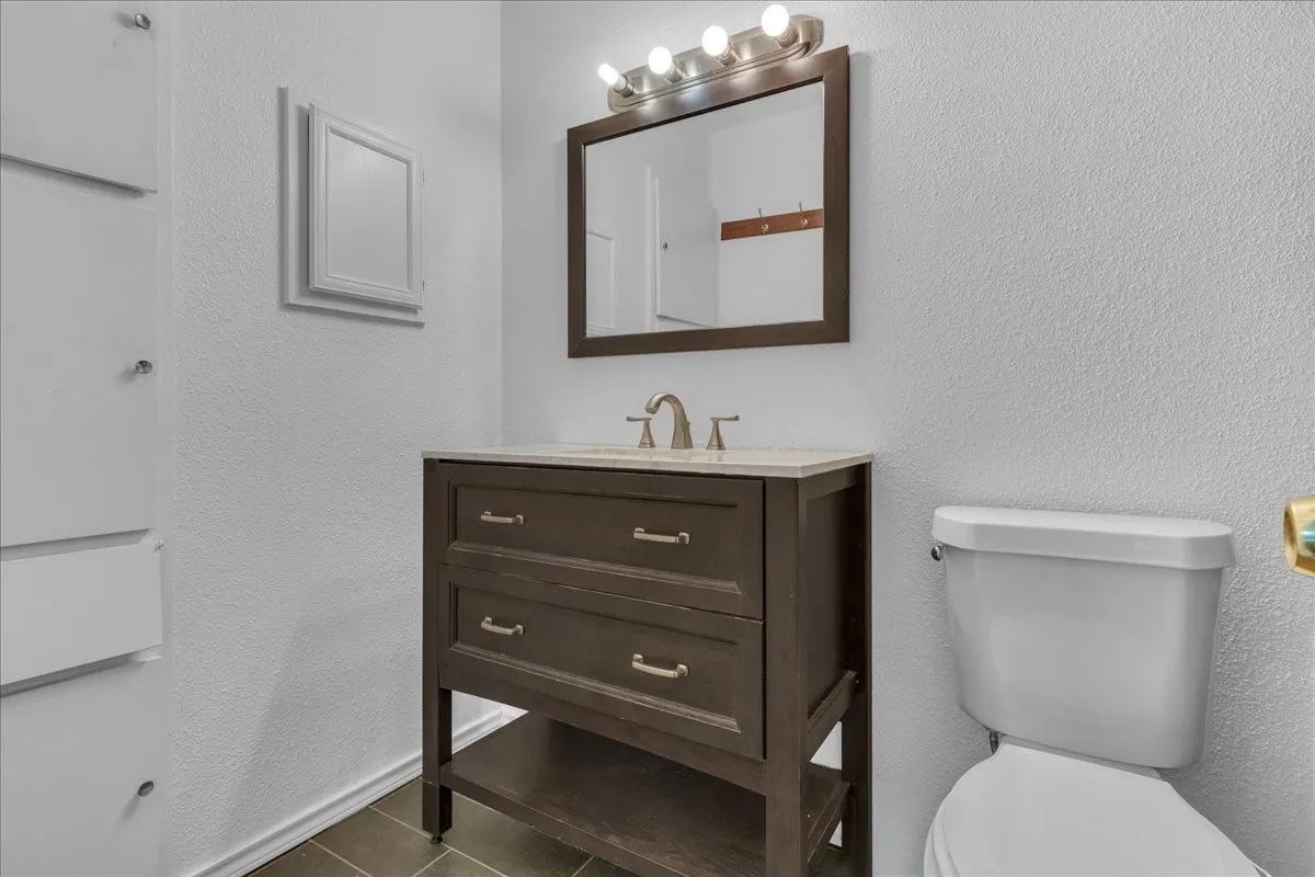 Half bathroom featuring a textured wall, vanity, and dark tile patterned floors