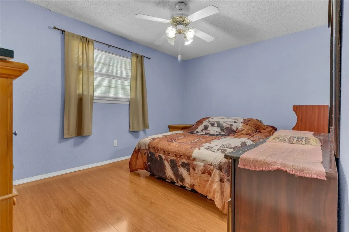Bedroom with light wood-style floors, ceiling fan, and a textured ceiling