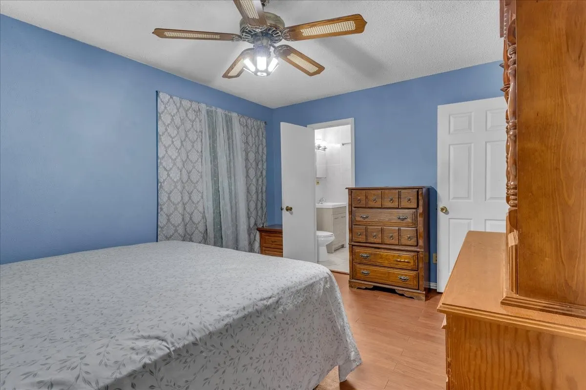 Bedroom with light wood-style flooring, a ceiling fan, ensuite bathroom, and a textured ceiling