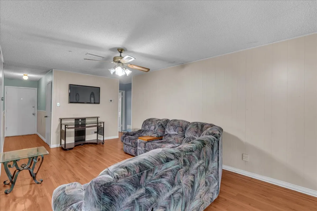 Living area with a ceiling fan, light wood-style floors, a textured ceiling, and wood walls