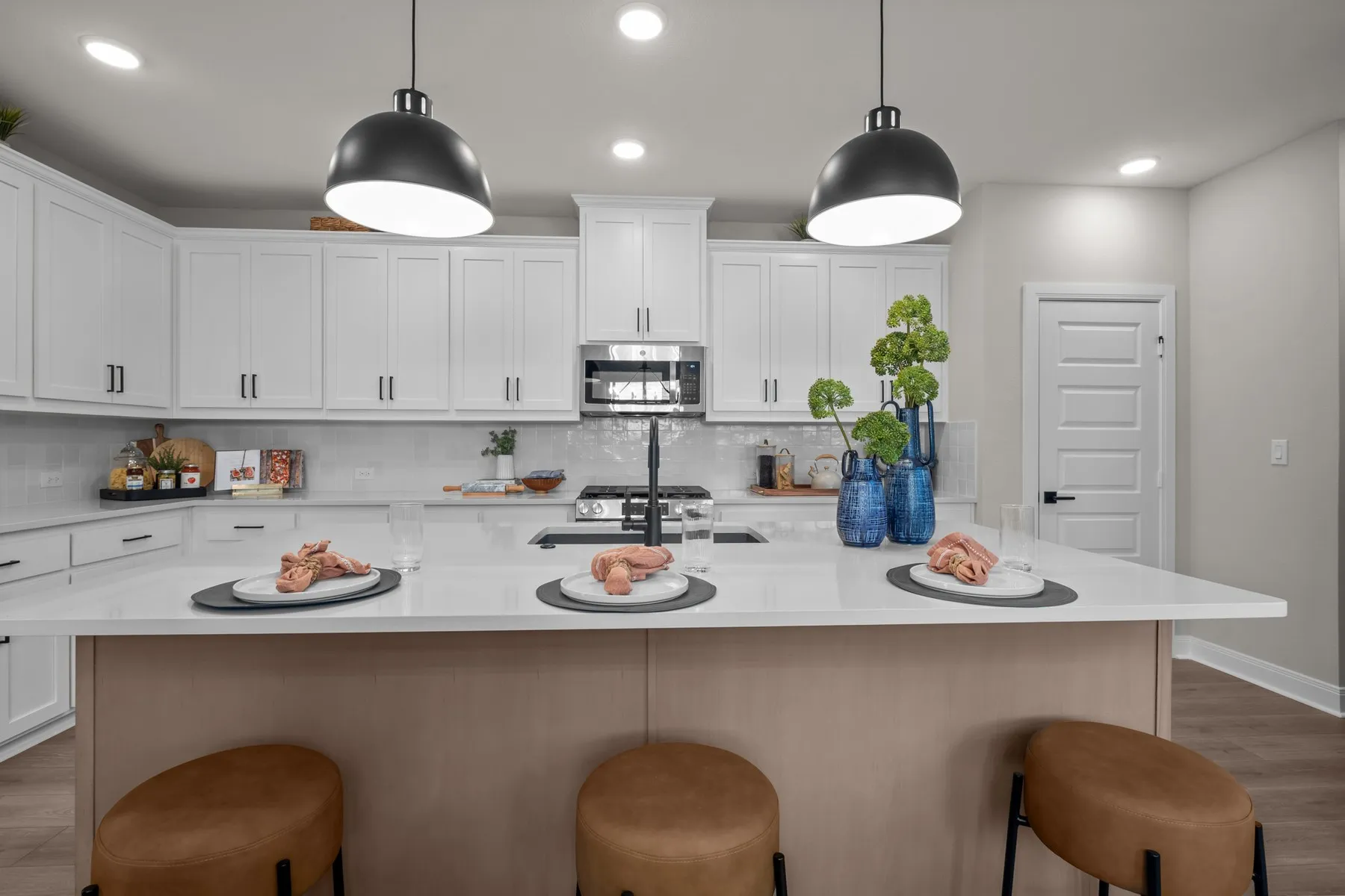 Kitchen featuring light wood finished floors, stainless steel appliances, a center island with sink, and hanging light fixtures