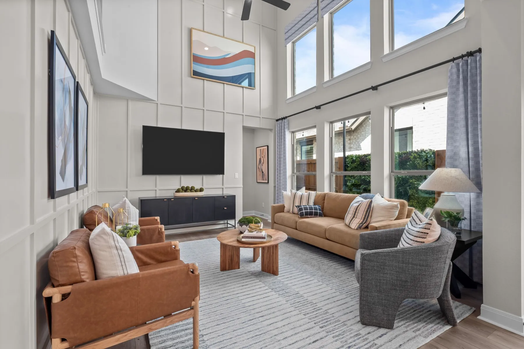 Living room with a decorative wall, light wood finished floors, a high ceiling, and a ceiling fan