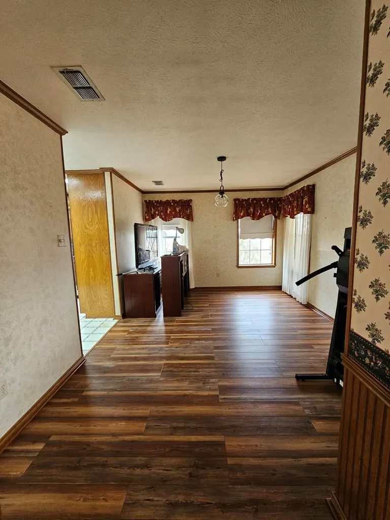 Unfurnished living room featuring wallpapered walls, ornamental molding, a textured ceiling, and dark wood-style floors