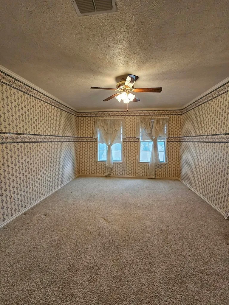 Carpeted spare room with wallpapered walls, a ceiling fan, a textured ceiling, and crown molding